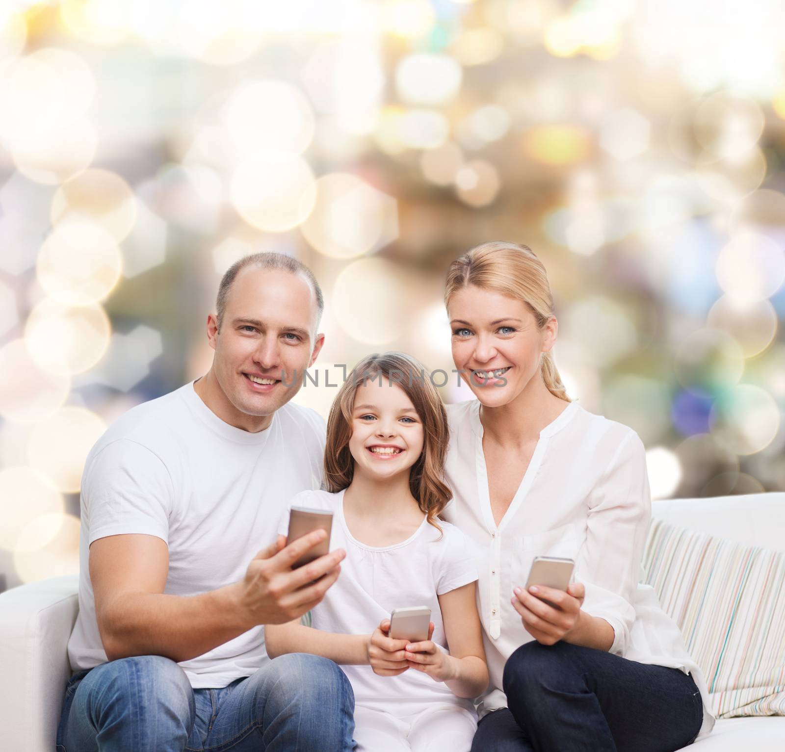 family, holidays, technology and people concept - smiling mother, father and little girl with smartphones over lights background