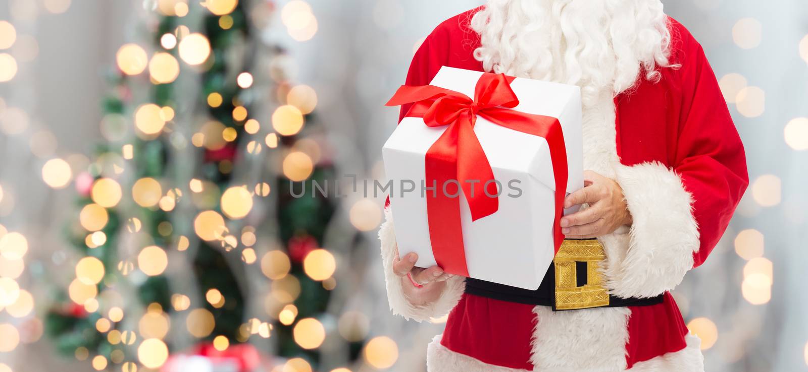christmas, holidays and people concept - close up of santa claus with gift box over tree lights background