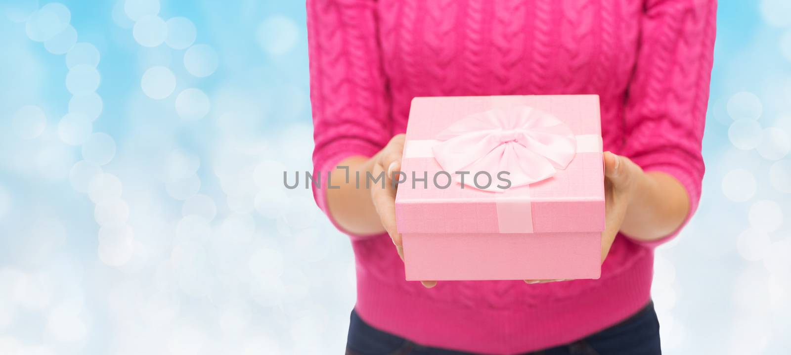 christmas, holidays and people concept - close up of woman in pink sweater holding gift box over blue lights background