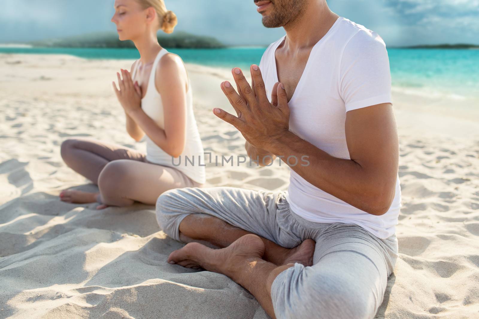 fitness, sport, yoga, people and lifestyle concept - happy couple sitting in lotus pose on beach