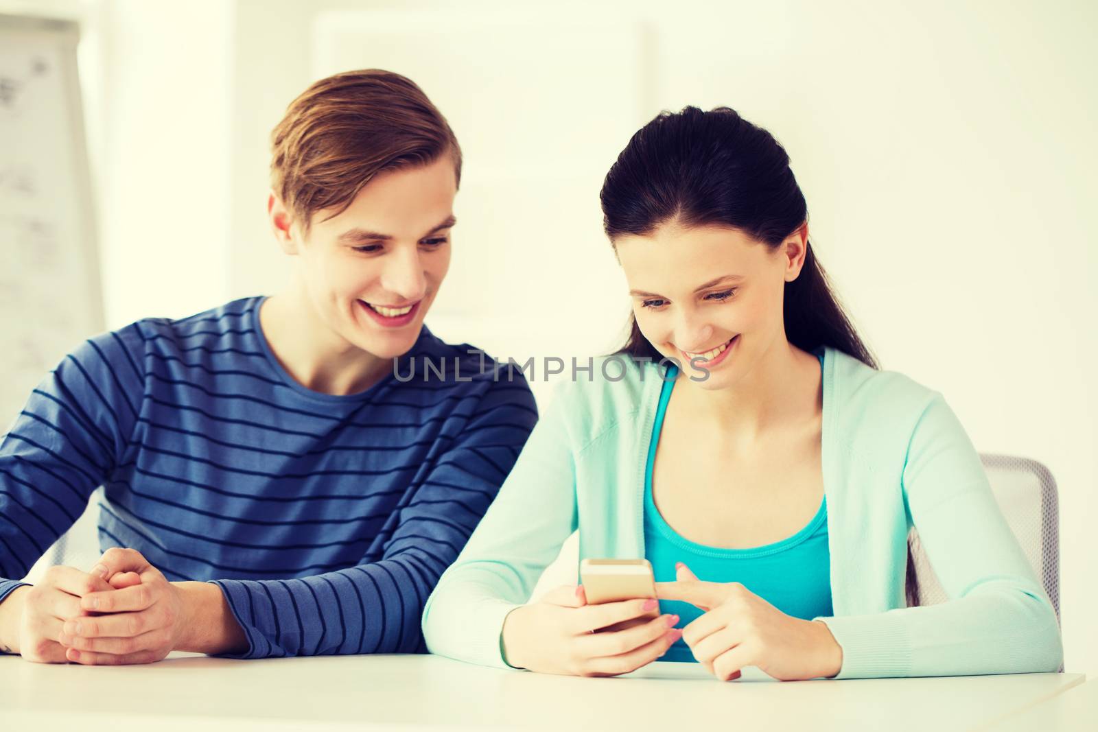 two smiling students with smartphone at school by dolgachov