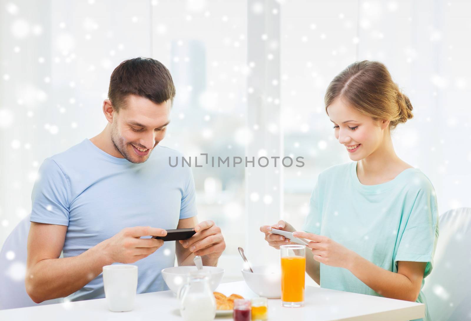 food, family, people and technology concept - smiling couple with smartphones and having breakfast at home