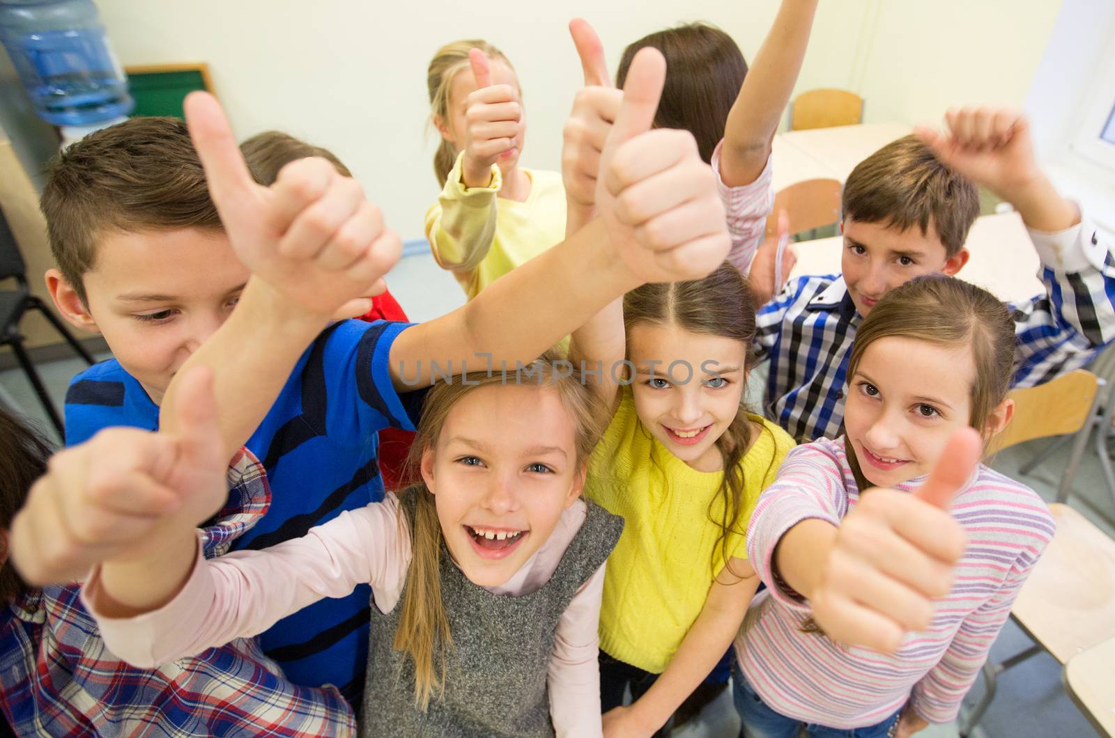 education, elementary school, learning, gesture and people concept - group of school kids and showing thumbs up in classroom