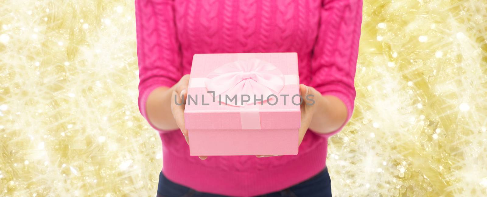 christmas, holidays and people concept - close up of woman in pink sweater holding gift box over yellow background