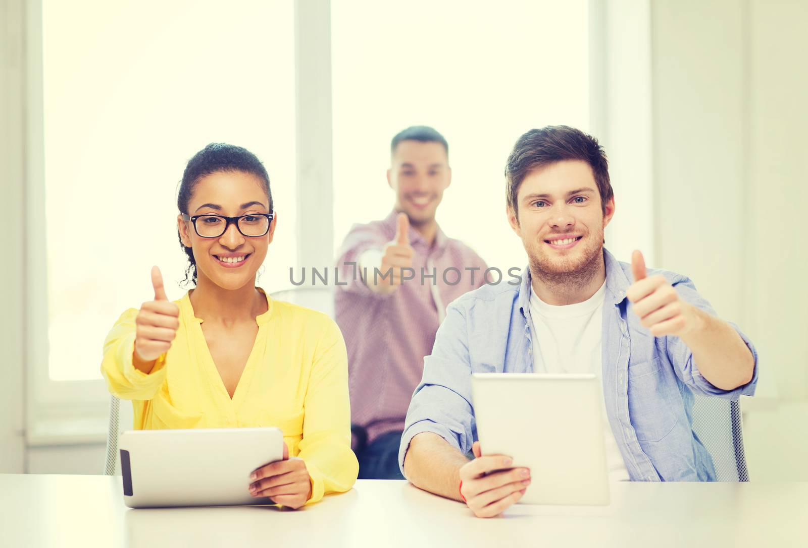 business, office and startup concept - creative smiling team with tablet pc computers at office showing thumbs up