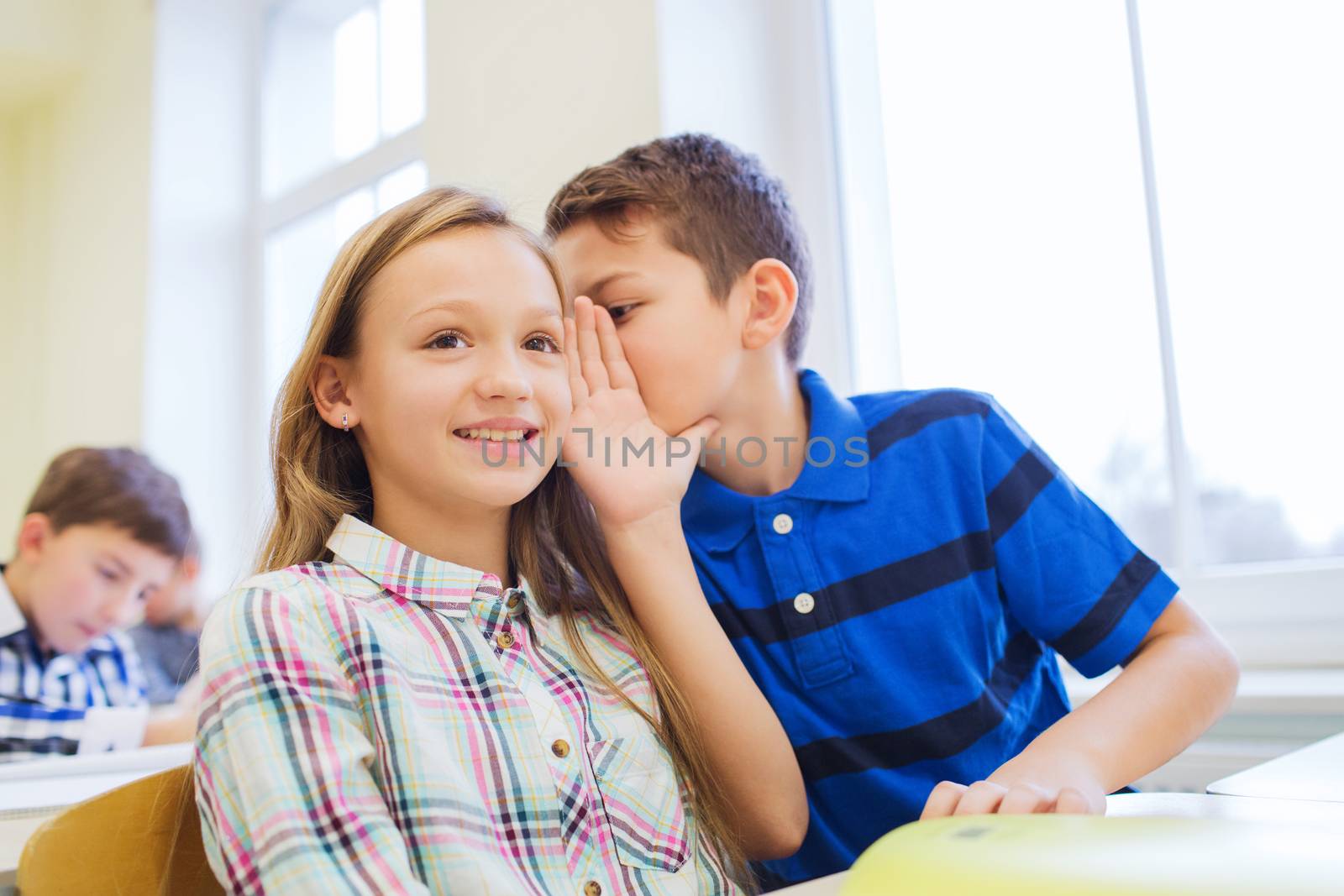 education, elementary school, learning and people concept - smiling schoolboy whispering secret to classmate ear in classroom