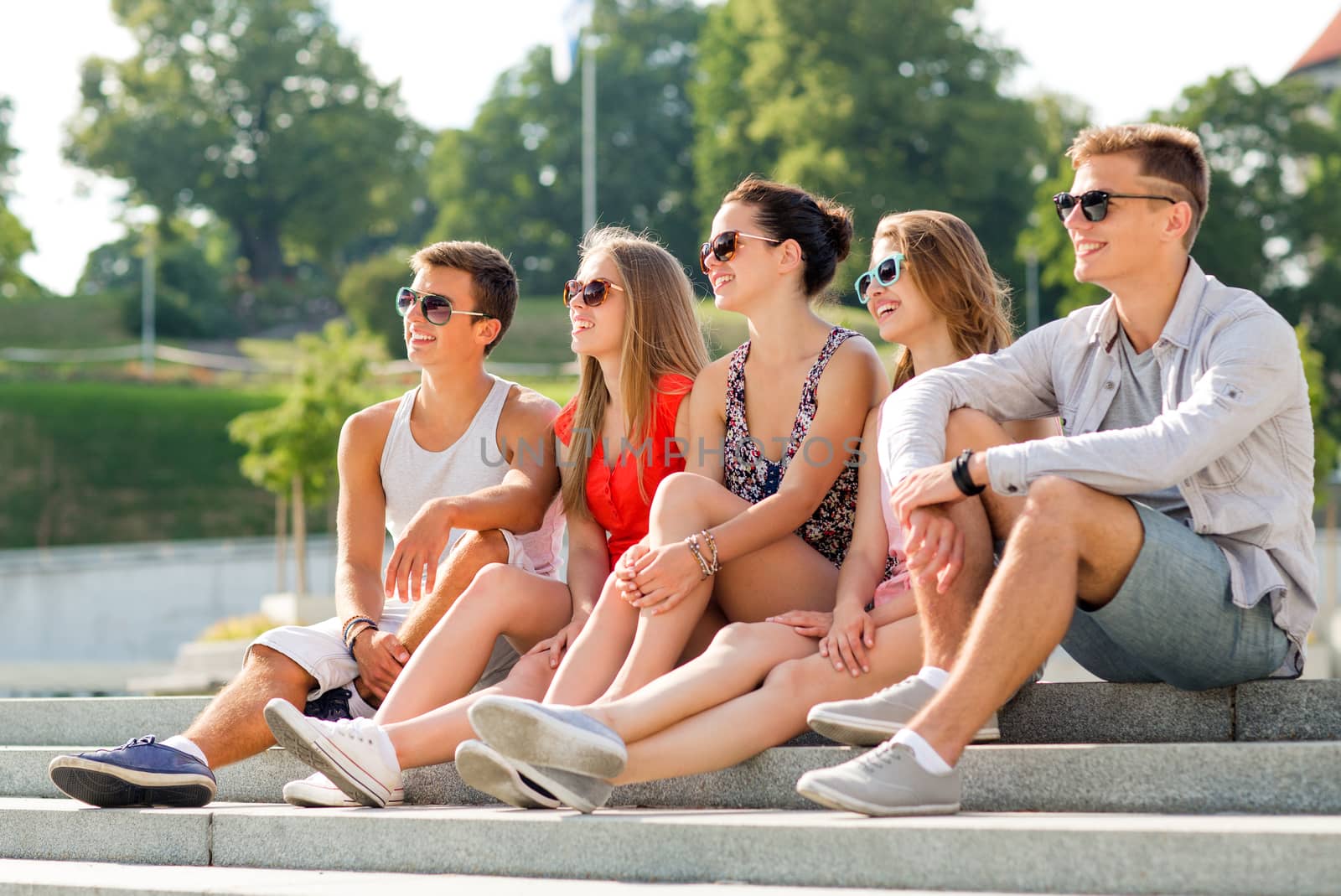 group of smiling friends sitting on city square by dolgachov