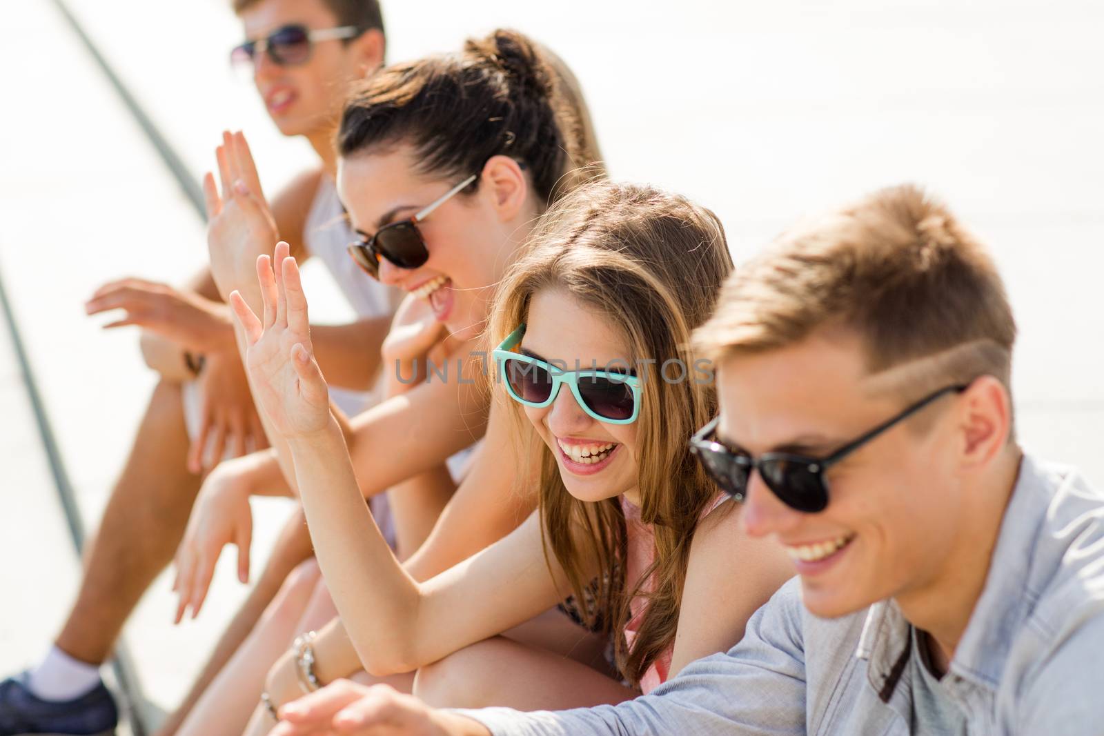 friendship, leisure, summer, gesture and people concept - group of laughing friends sitting on city square