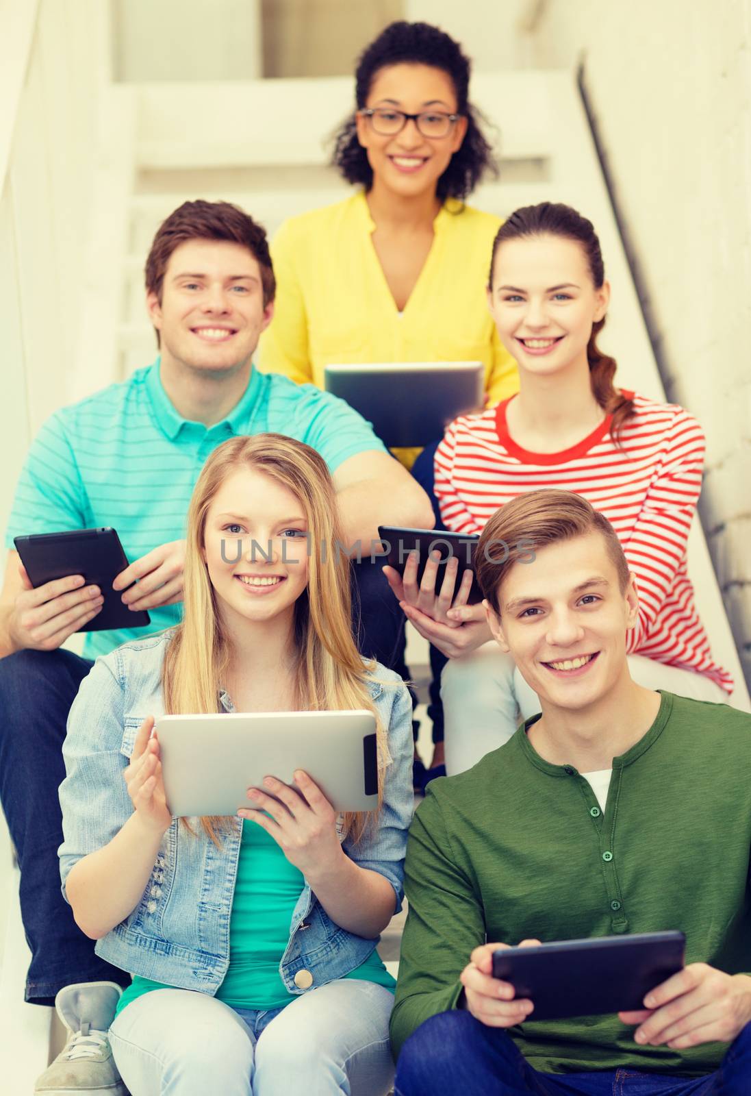 education and technology concept - smiling students with tablet pc computer sitting on staircase