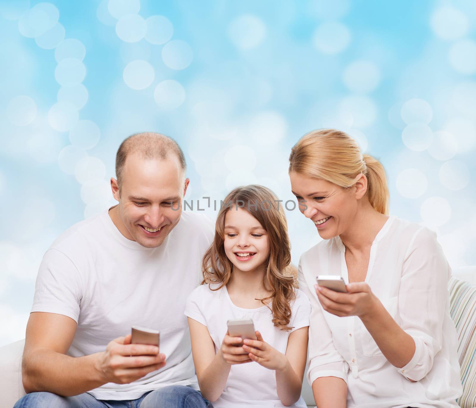 family, holidays, technology and people - smiling mother, father and little girl with smartphones over blue lights background