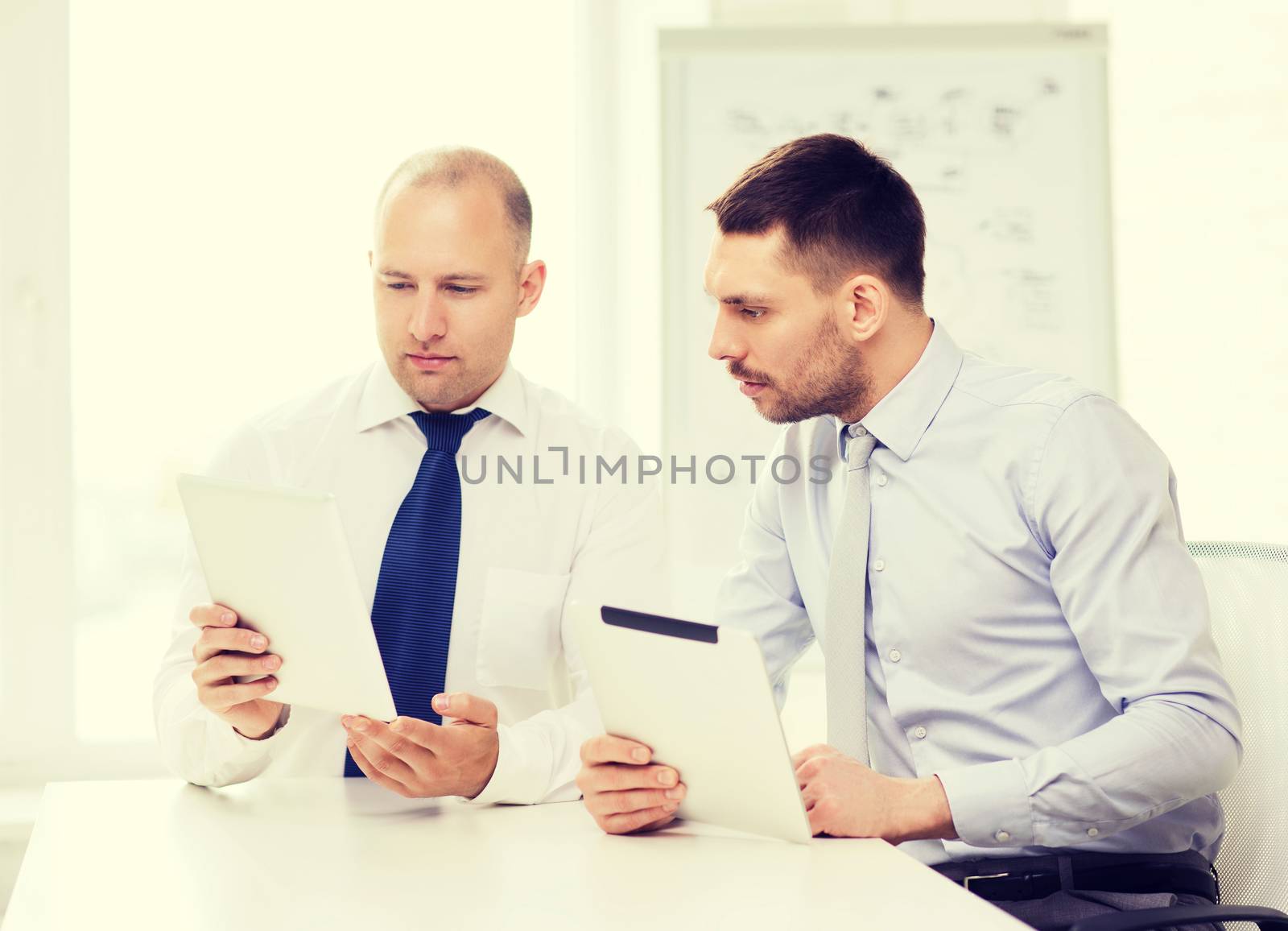business, technology and office concept - two serious businessmen with tablet pc computers in office