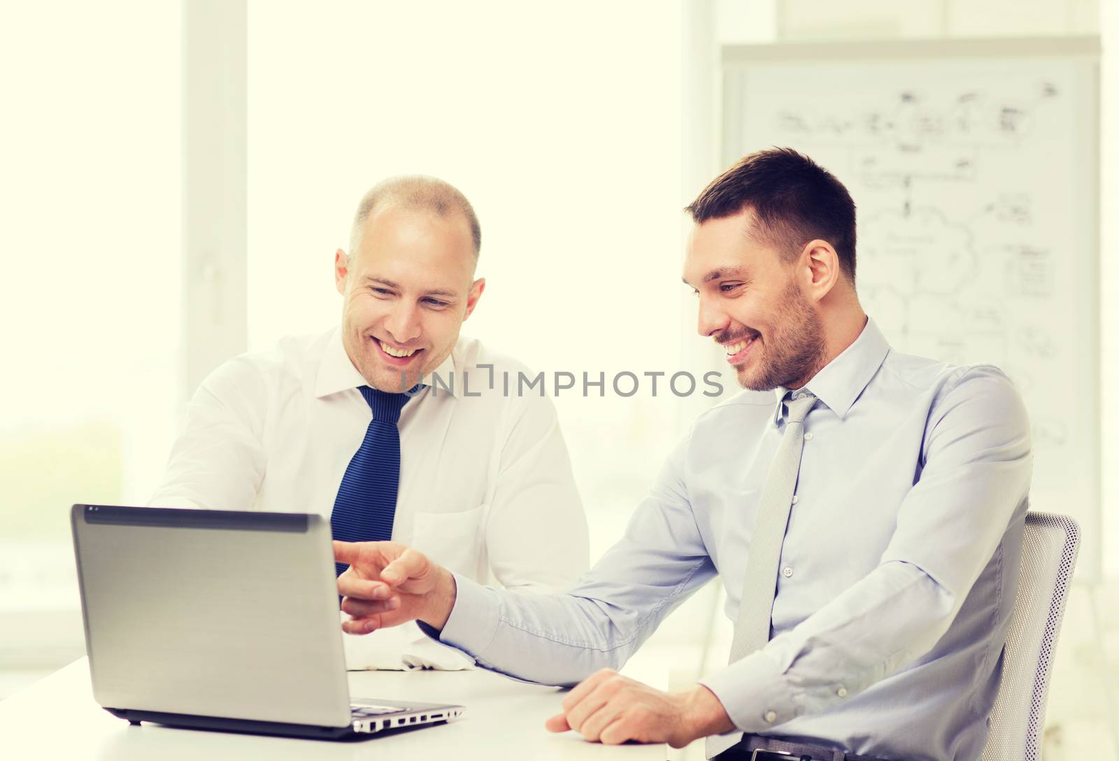 business, technology and office concept - two smiling businessmen with laptop in office