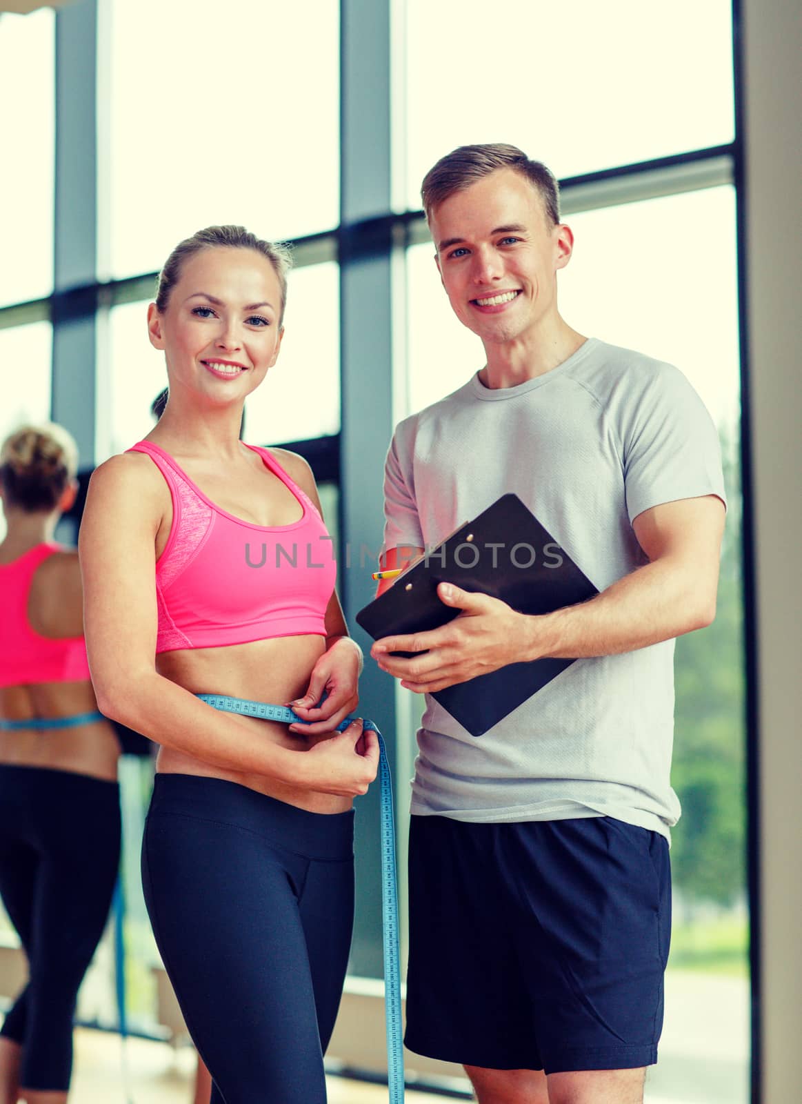smiling young woman with personal trainer in gym by dolgachov