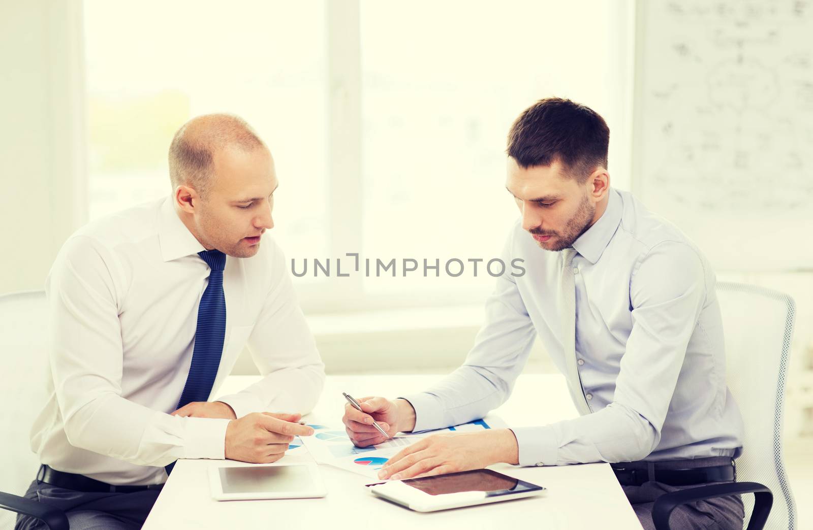 business, technology and office concept - two serious businessmen with tablet pc computers and files in office