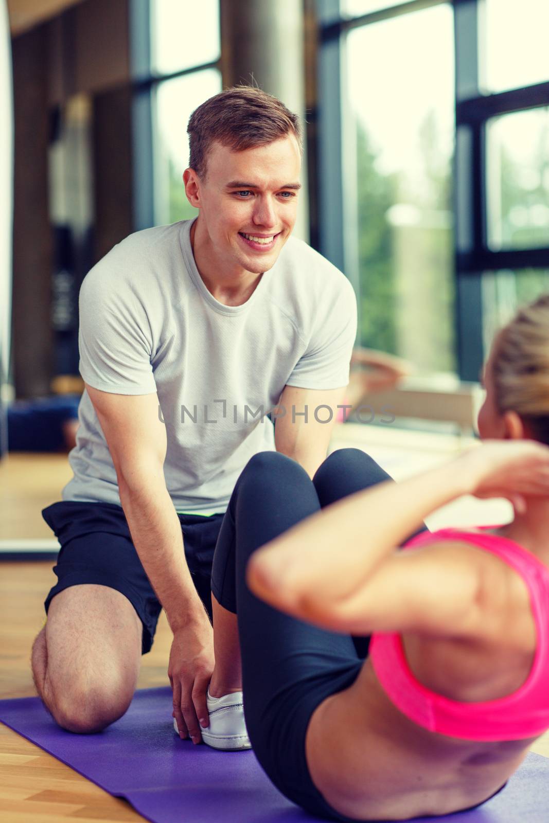 smiling woman with male trainer exercising in gym by dolgachov