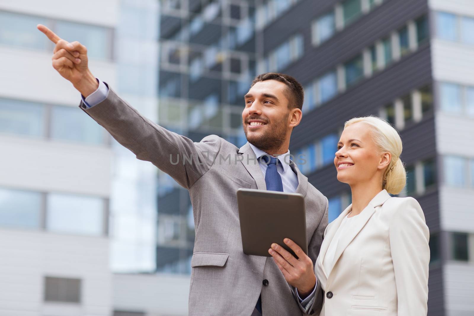 business, partnership, technology and people concept - smiling businessman and businesswoman with tablet pc computer over office building