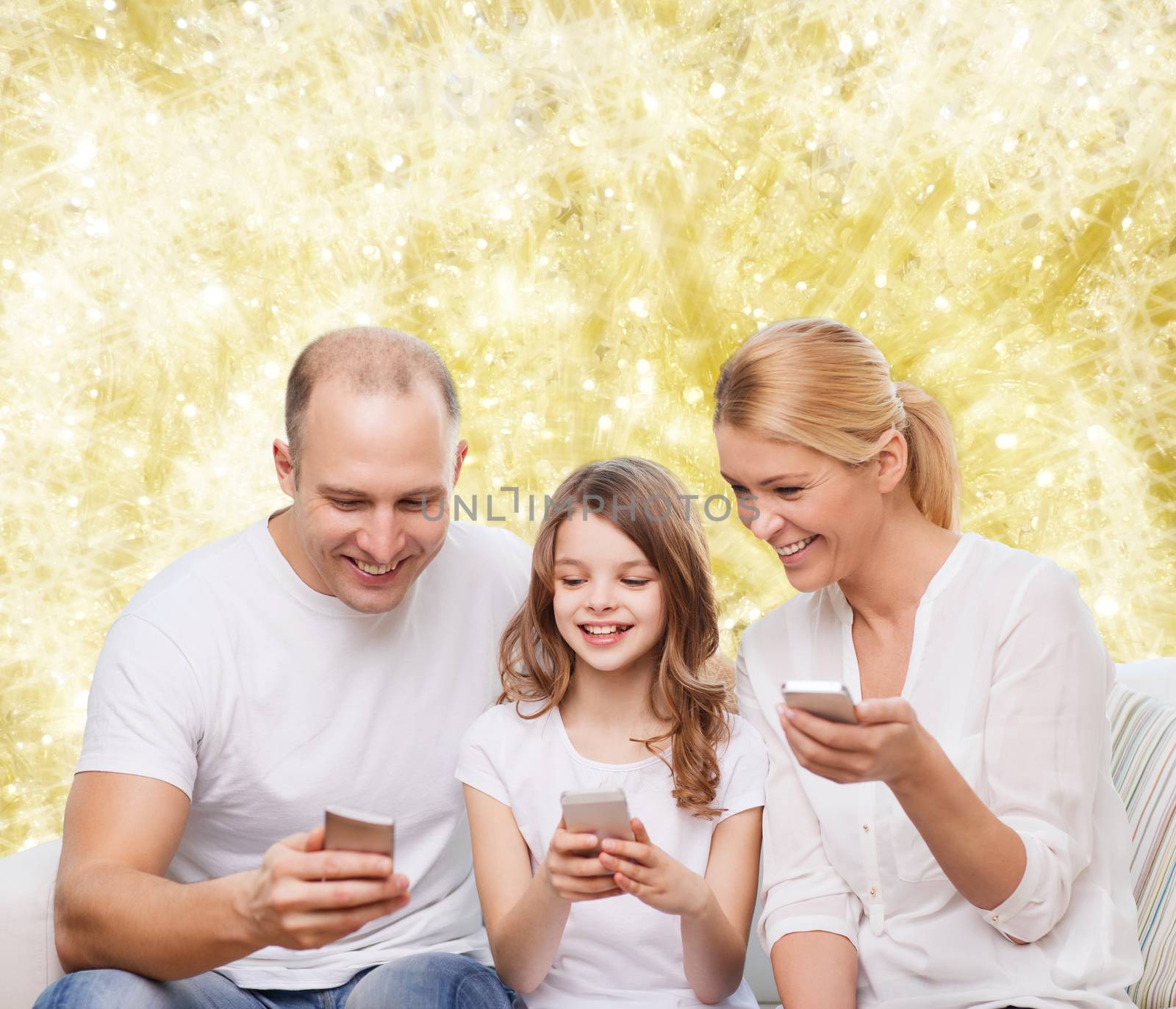 family, holidays, technology and people - smiling mother, father and little girl with smartphones over yellow lights background