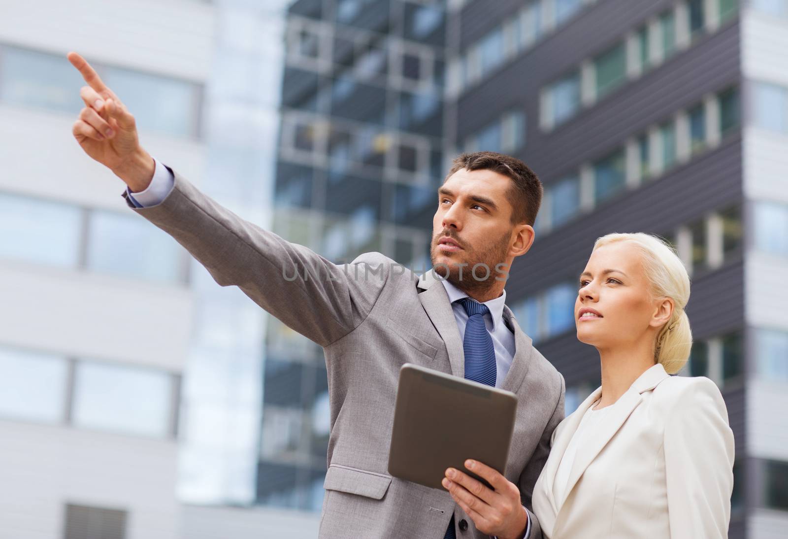 business, partnership, technology and people concept - serious businessman and businesswoman with tablet pc computer over office building