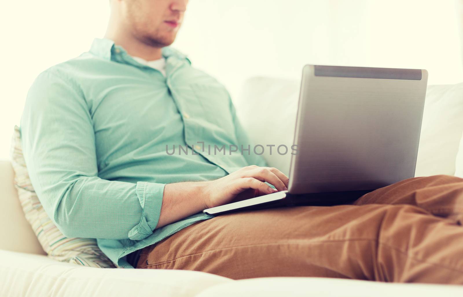 technology, home and lifestyle concept - close up of man working with laptop computer and sitting on sofa at home