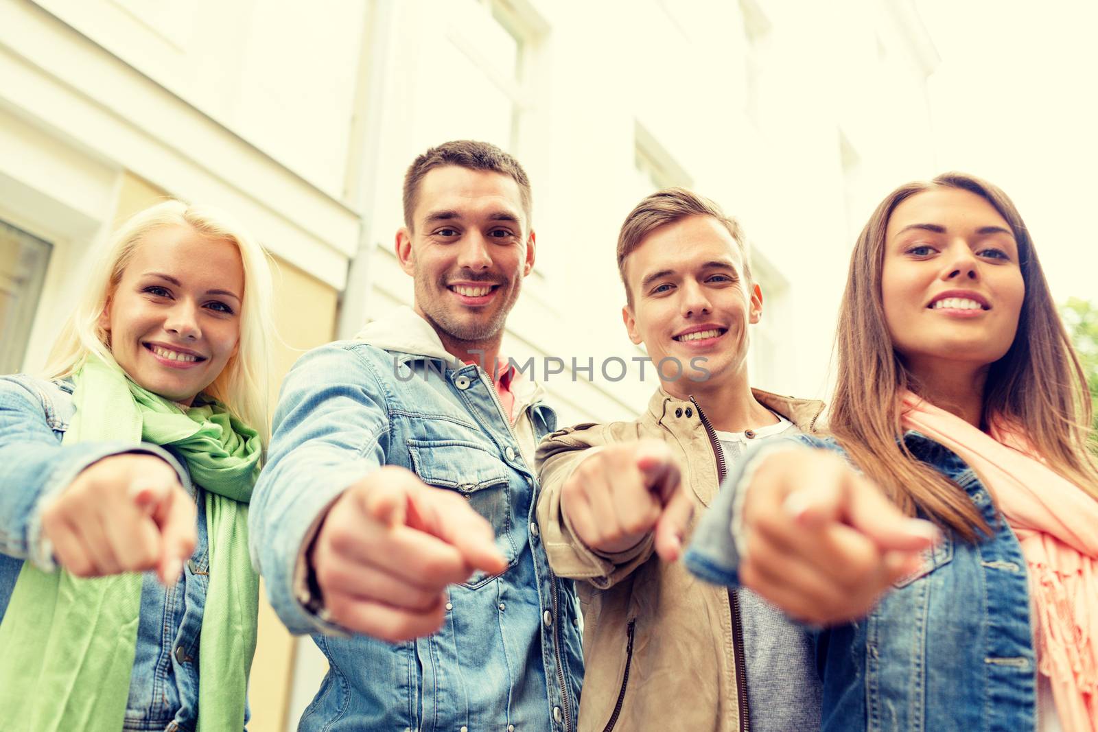 group of smiling friends in city pointing finger by dolgachov