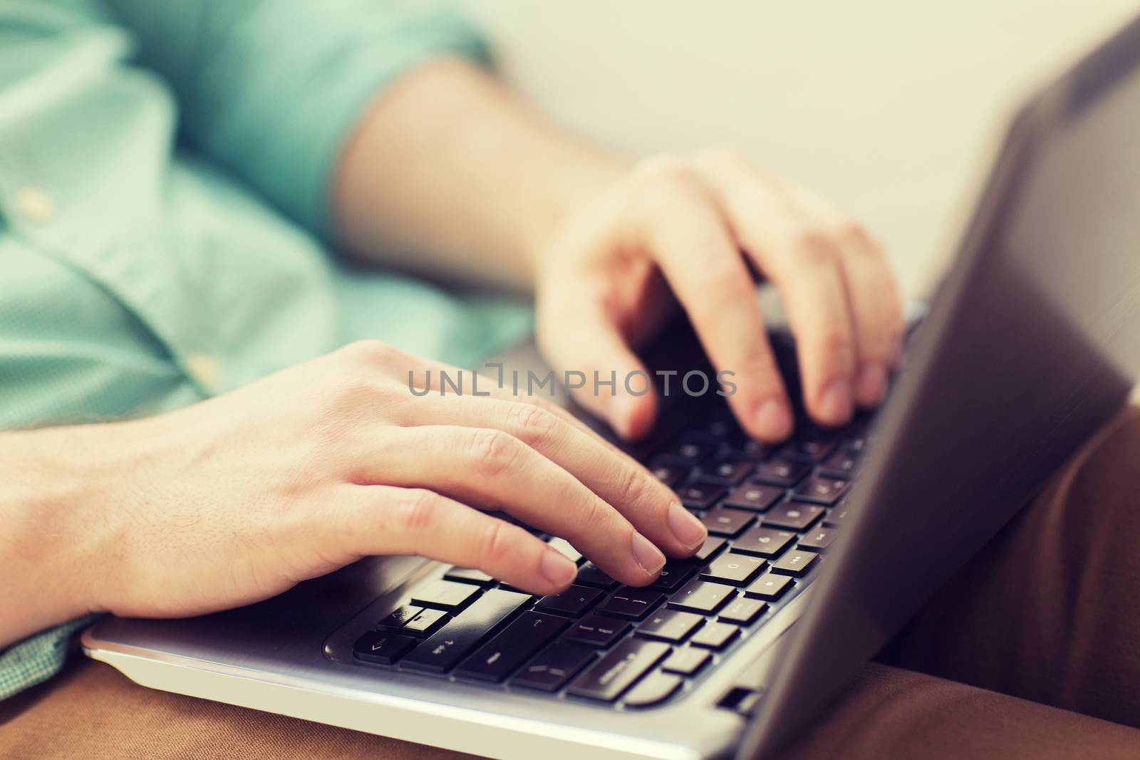 technology, home and lifestyle concept - close up of man working with laptop computer and sitting on sofa at home