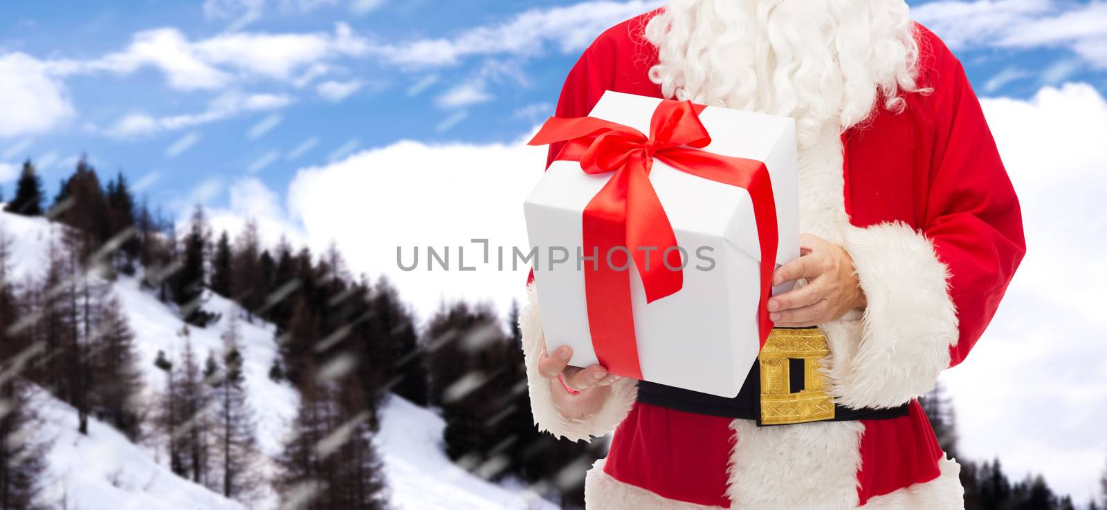 christmas, holidays and people concept - close up of santa claus with gift box over snowy mountains