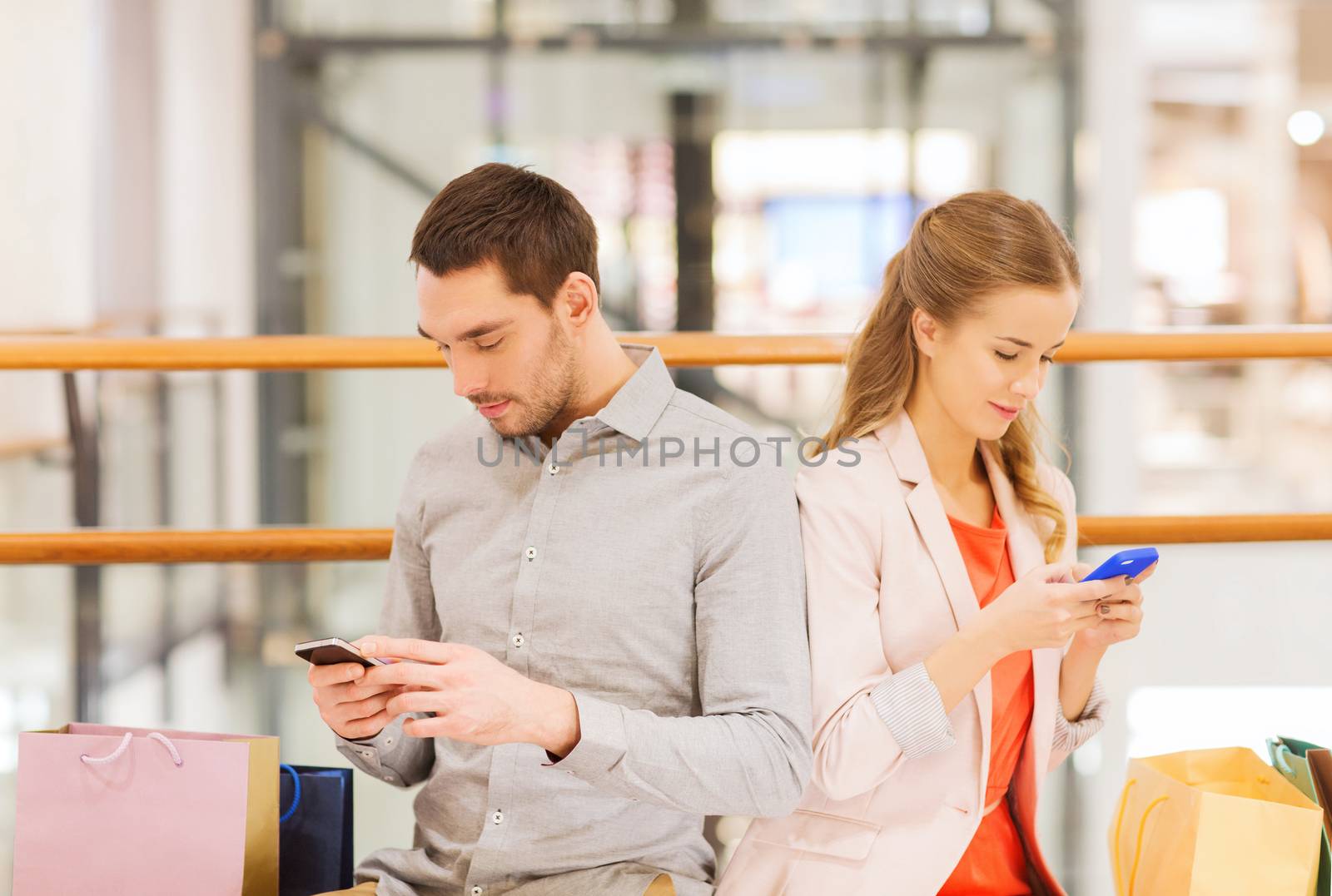 couple with smartphones and shopping bags in mall by dolgachov