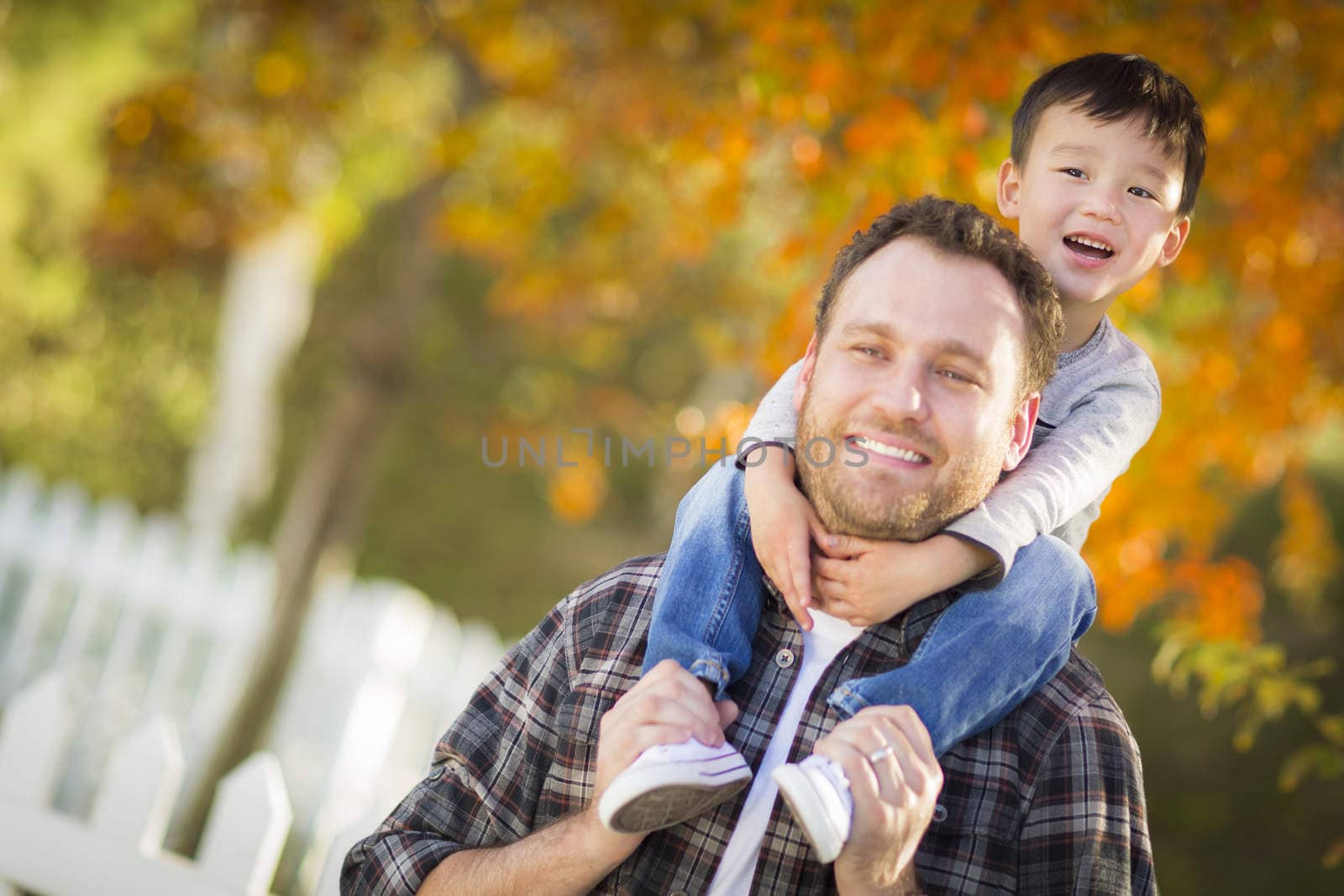 Happy Mixed Race Boy Riding Piggyback on Shoulders of Caucasian Father.