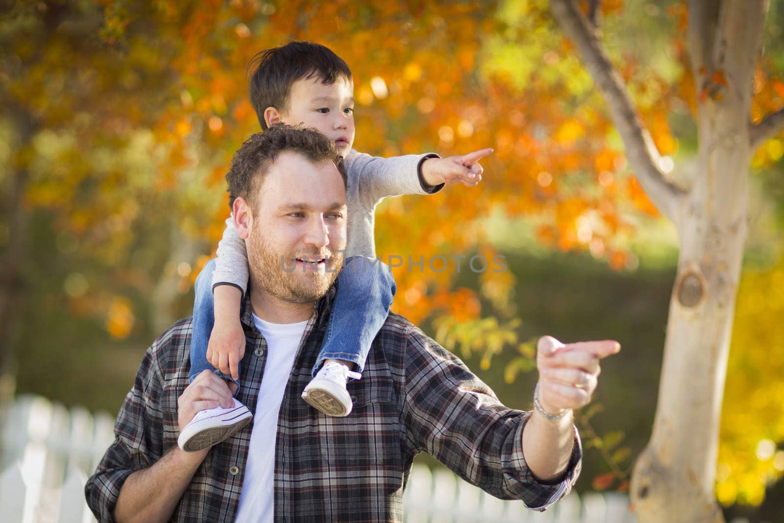 Happy Mixed Race Boy Riding Piggyback and Pointing on Shoulders of Caucasian Father.