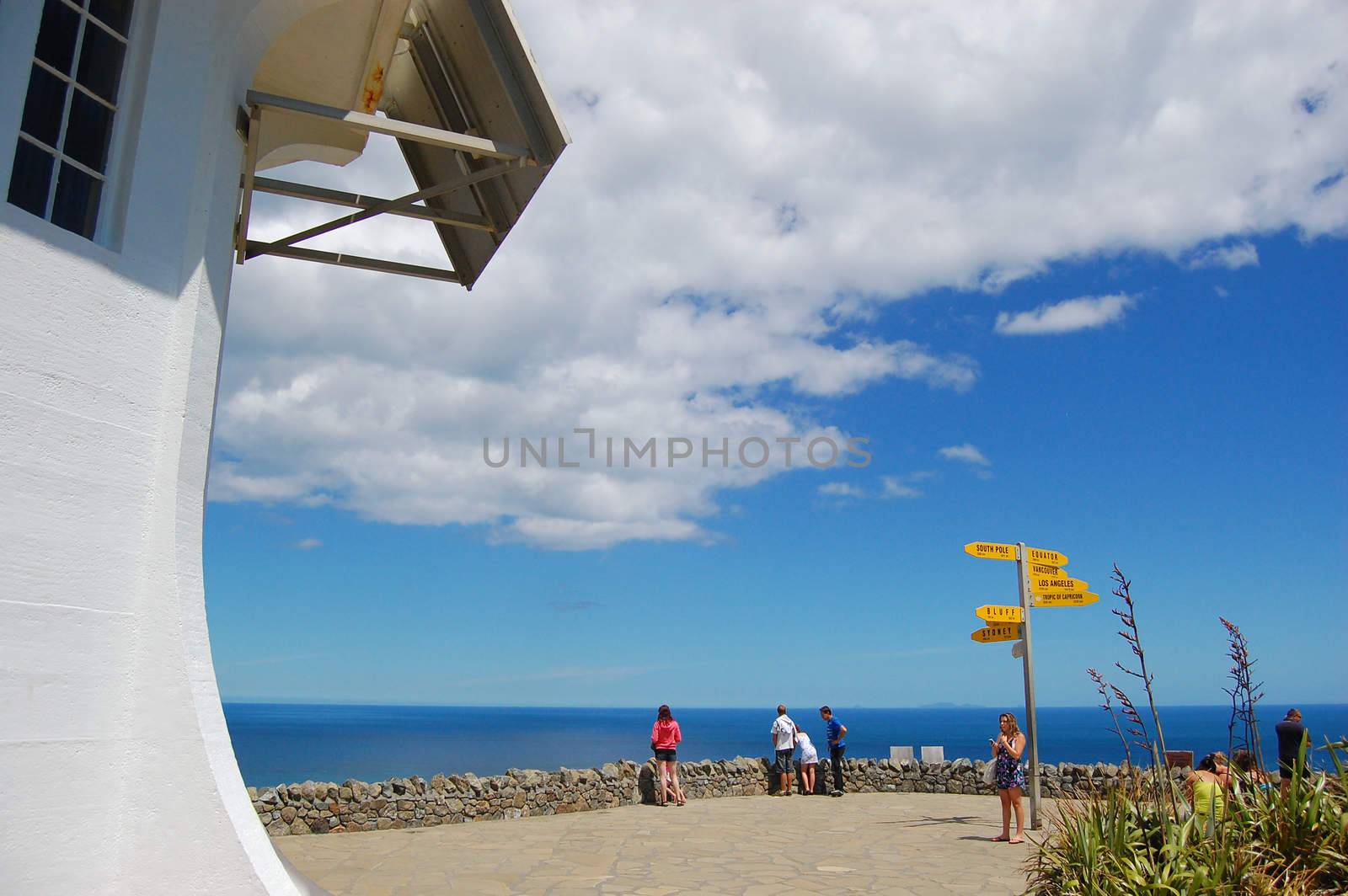 People at Cape Reinga lighthouse direction signs by danemo