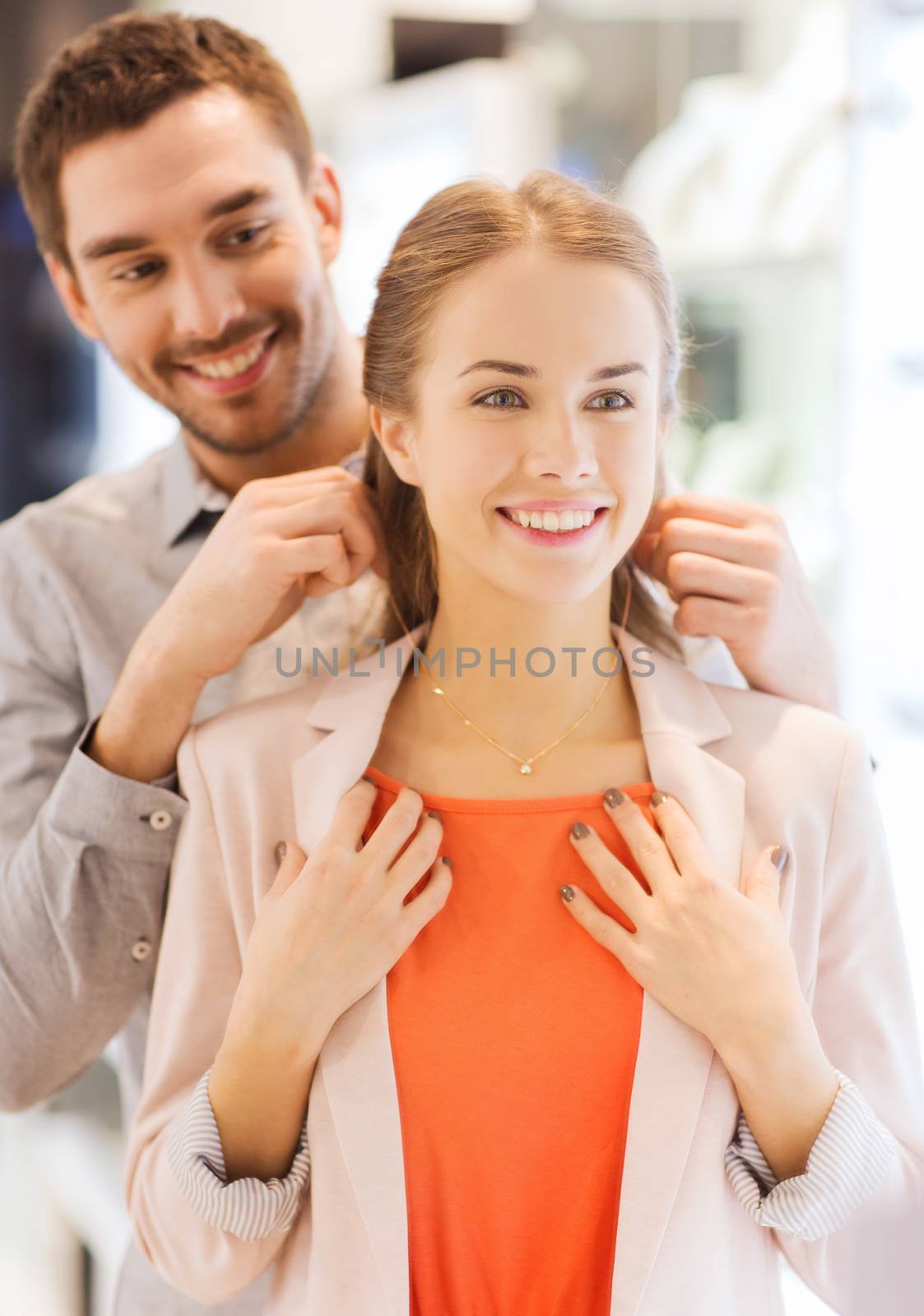 couple trying golden pendant on at jewelry store by dolgachov