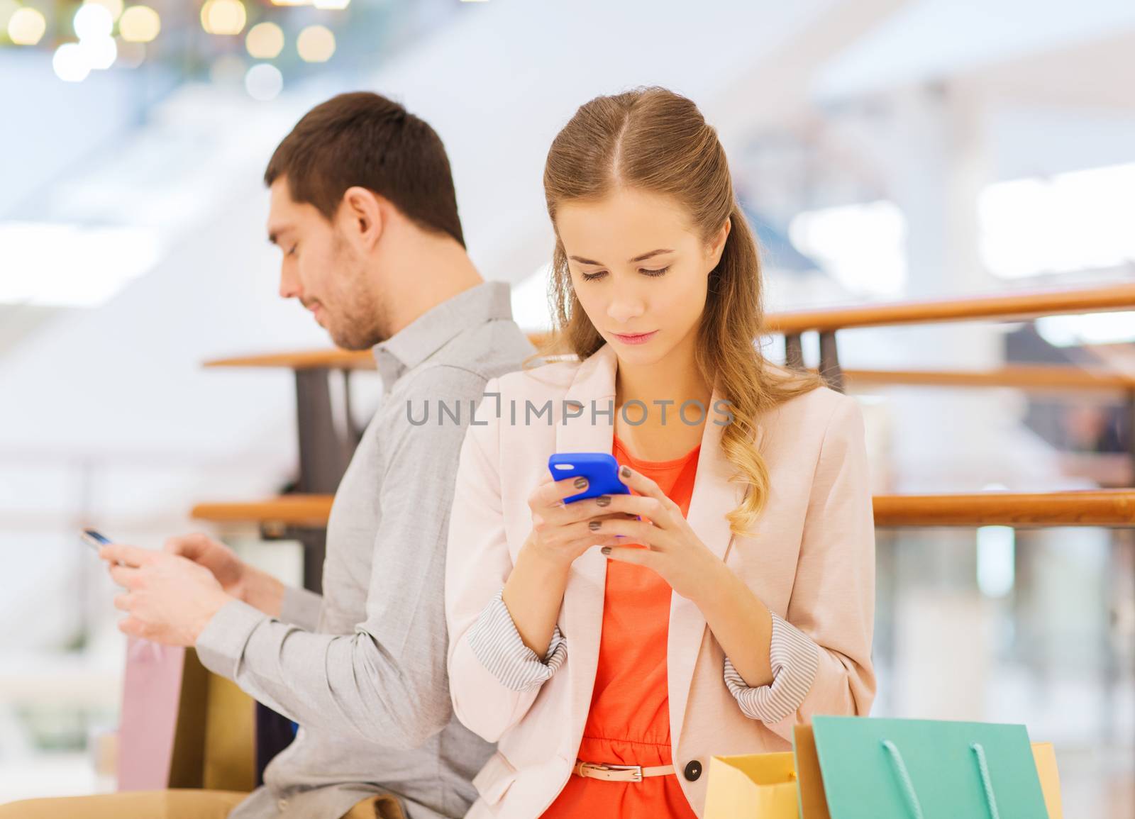 couple with smartphones and shopping bags in mall by dolgachov