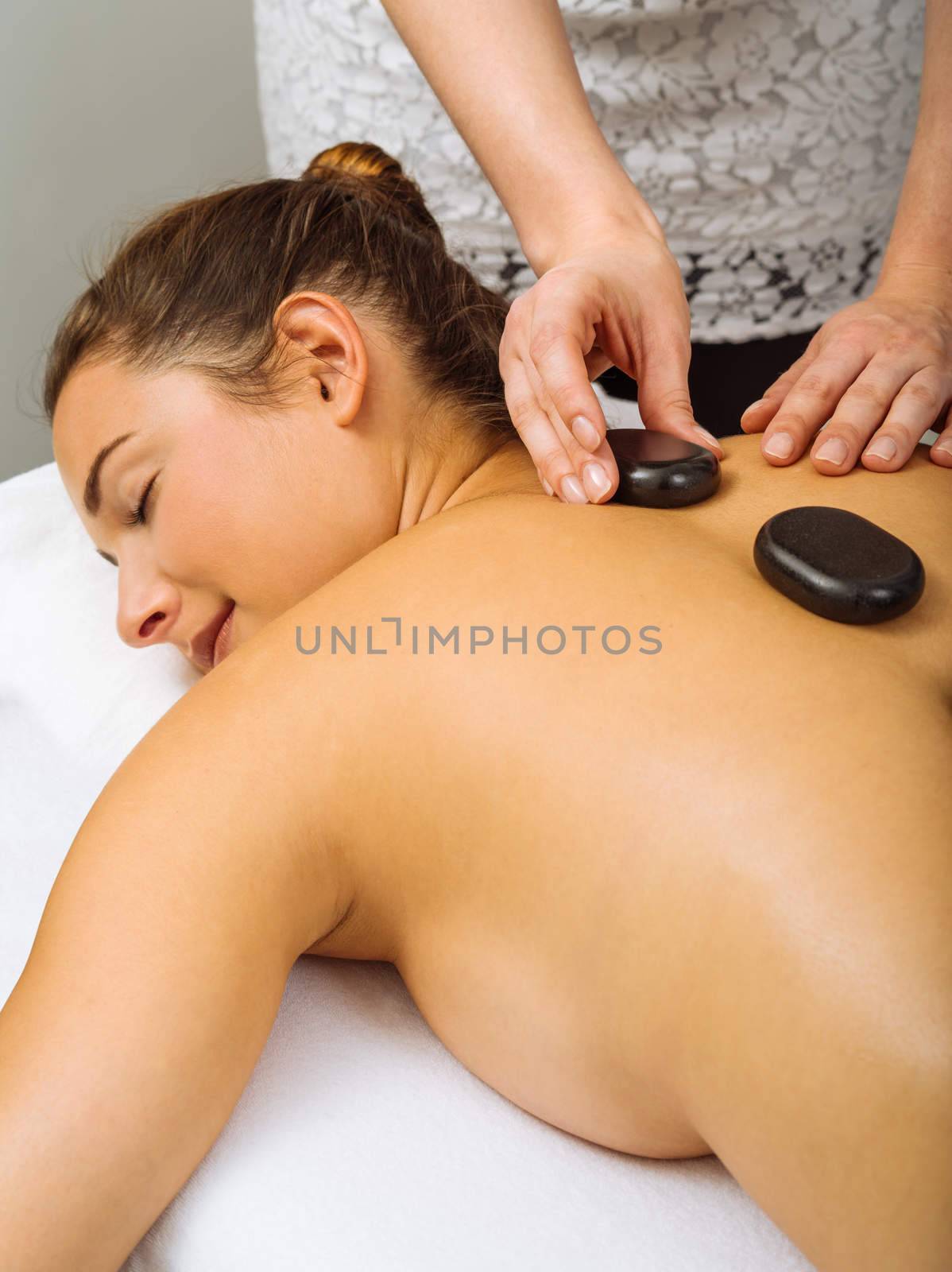 Photo of a young woman lying in a spa having a hot stone treatment. Focus on the hands.