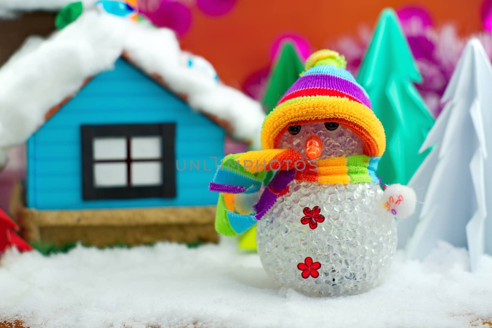 Snowman on snow with christmas tree and small house background.