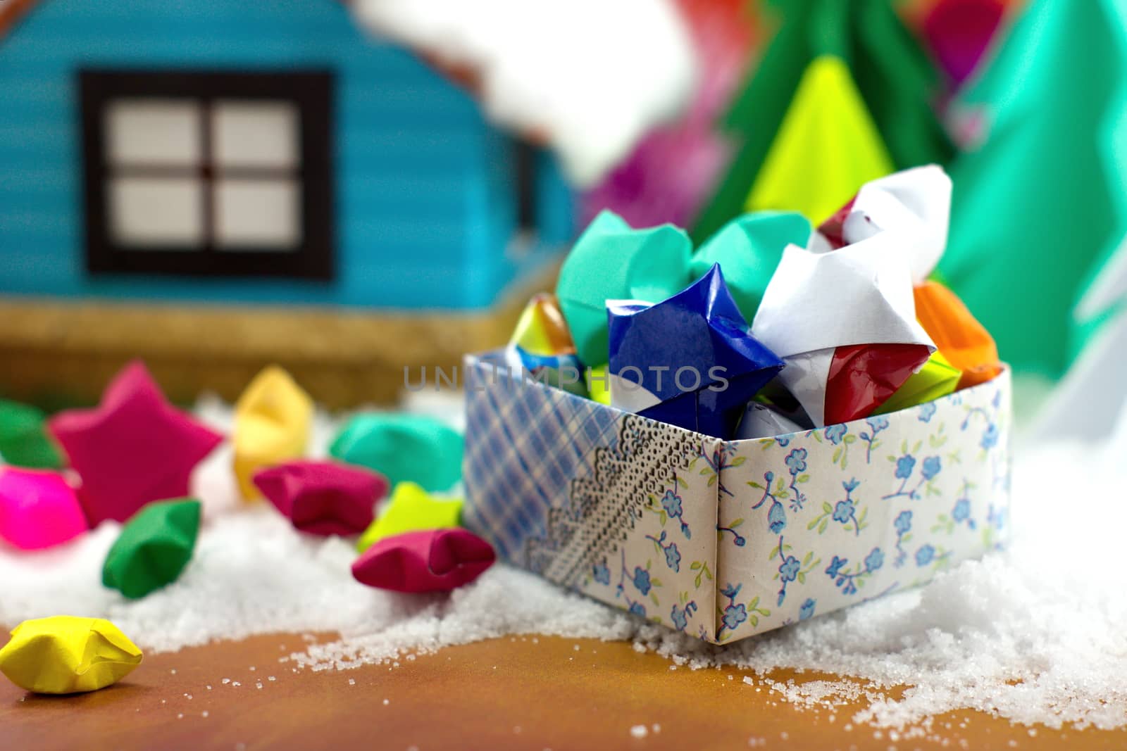 Paper stars in a gift box on the snow, with the small house and Christmas tree background