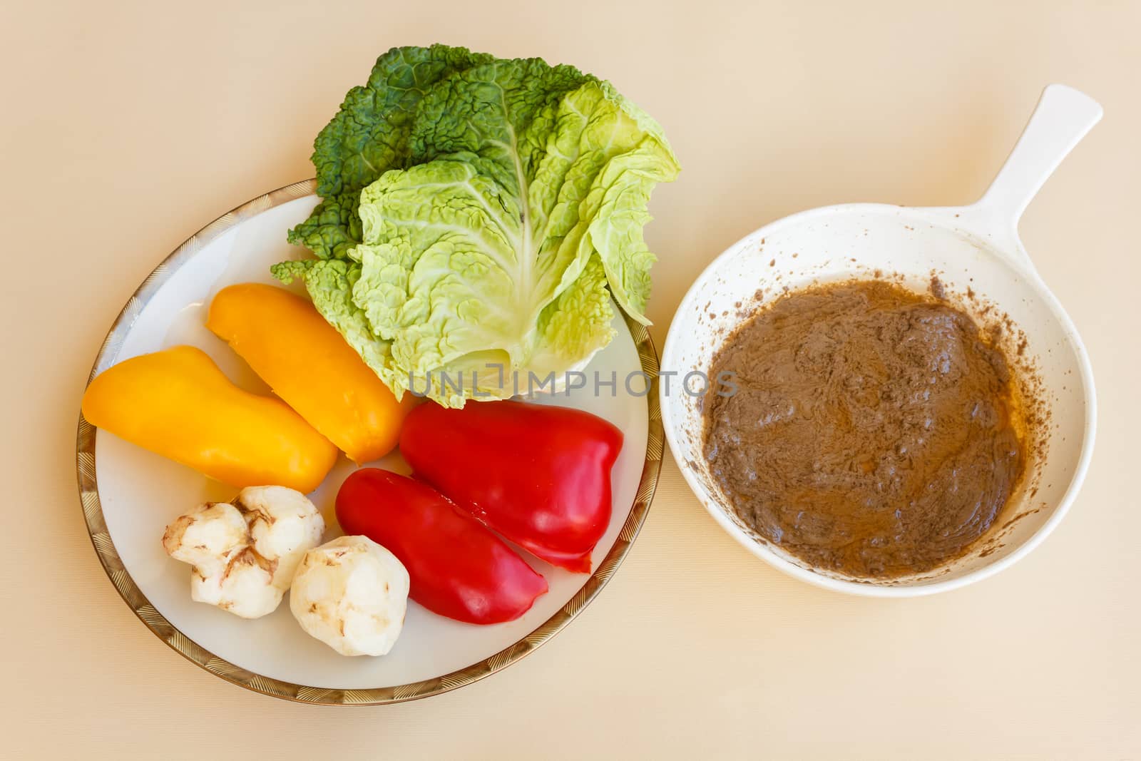 pan of bagna cauda with a plate of red and yellow peppers ,green cabbage and topinambour serving as trimming