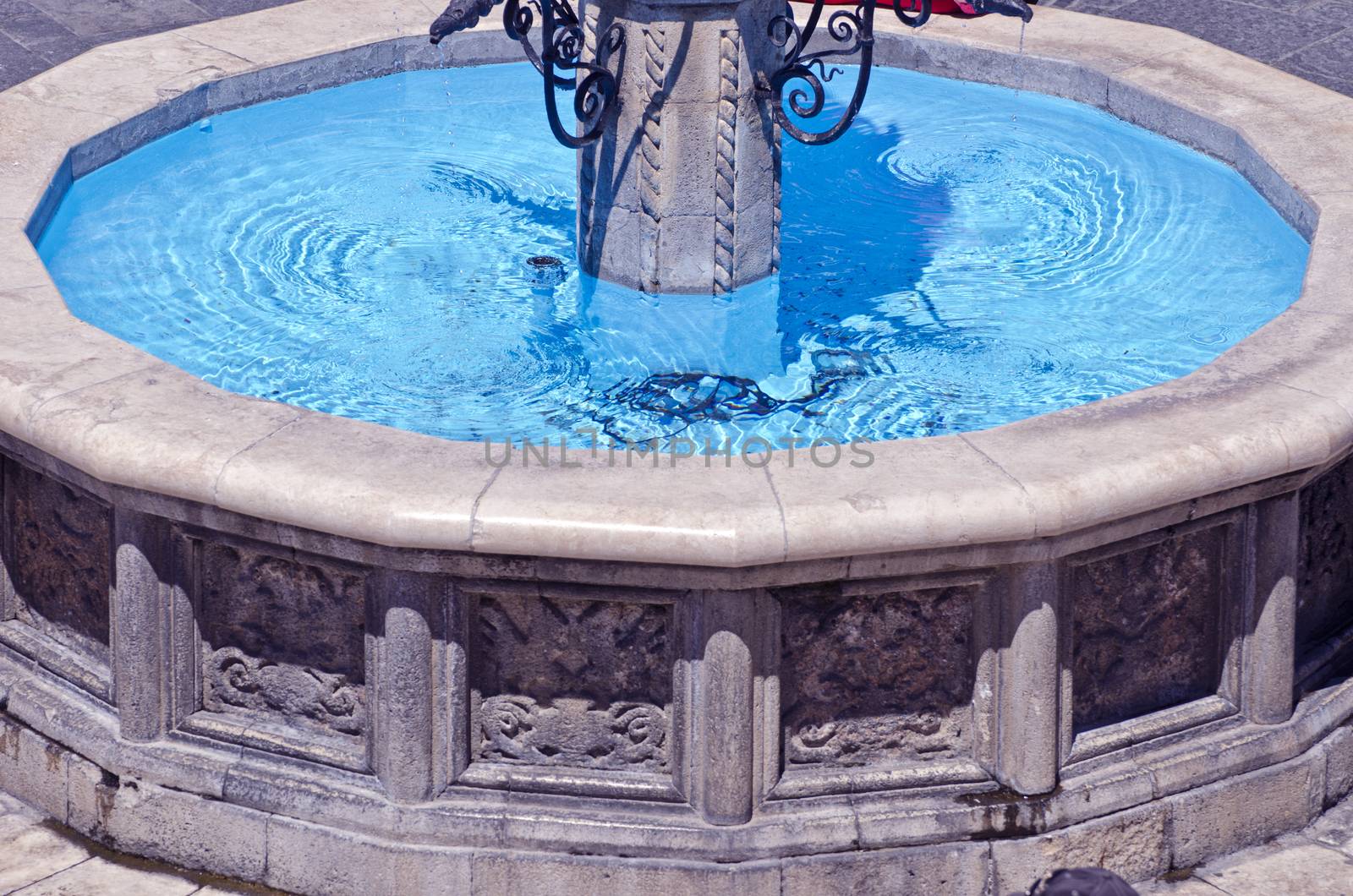 Antique stone fountain with blue water on sunny day, Greece