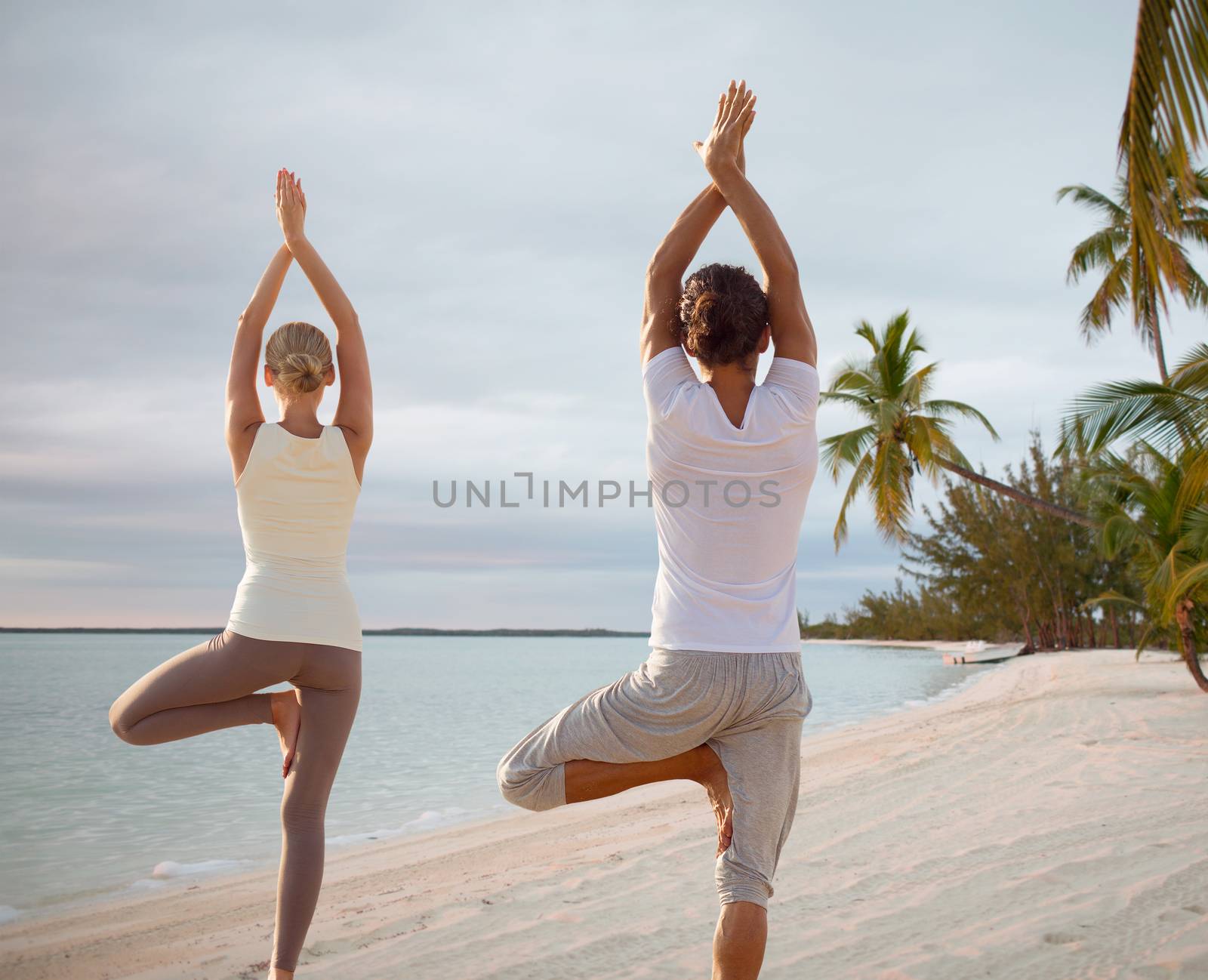 couple making yoga exercises on beach from back by dolgachov