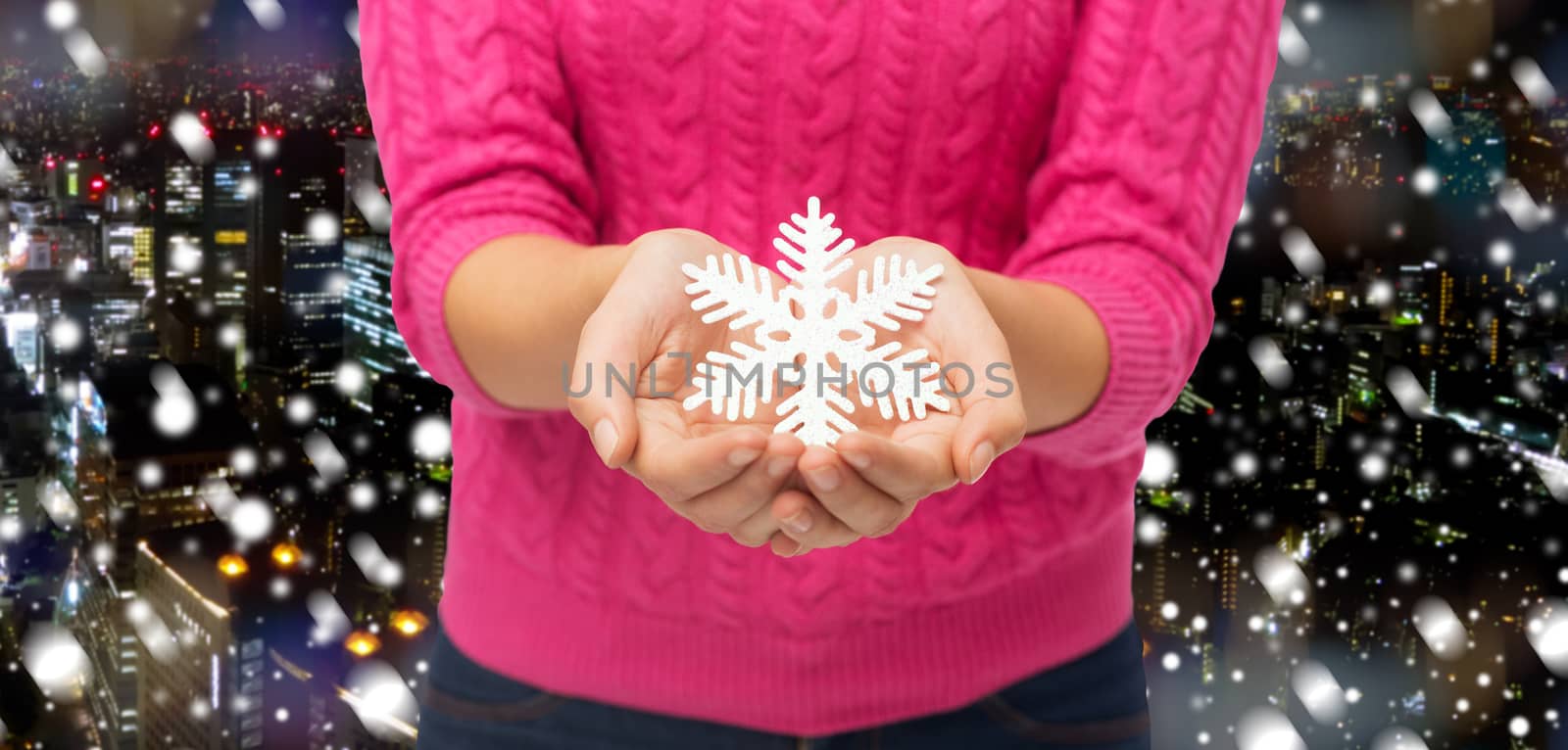 christmas, winter, holidays and people concept - close up of woman in pink sweater holding snowflake decoration over snowy night city background