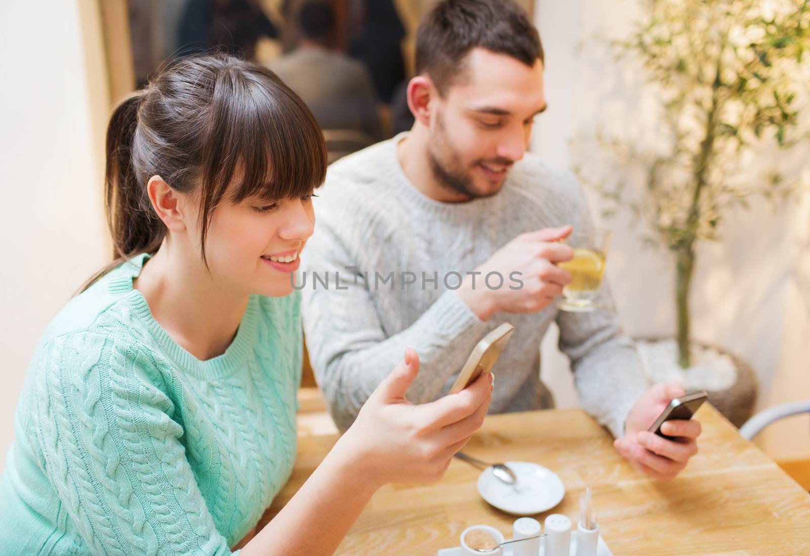 people, leisure, friendship and technology concept - smiling couple with smartphones meeting and drinking tea at cafe