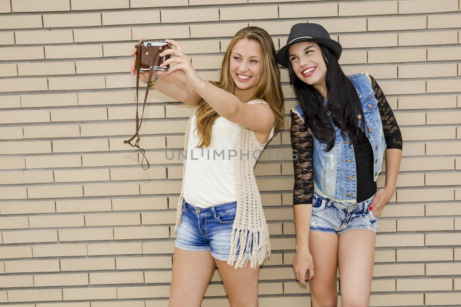 Two beautiful and young girlfriends taking pictures with a vintage camera