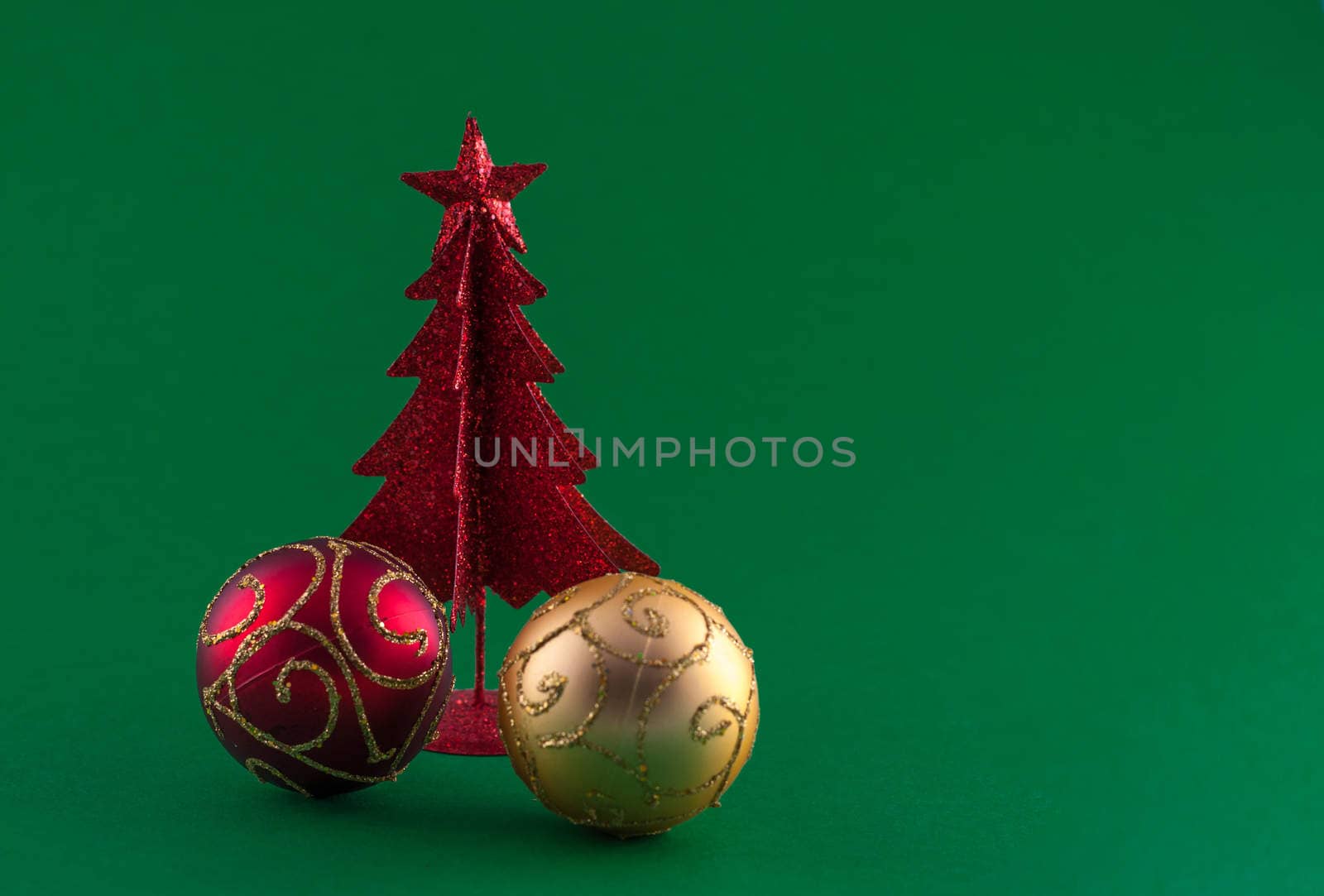 Little, red metallic christmas tree with tree adornments on green background