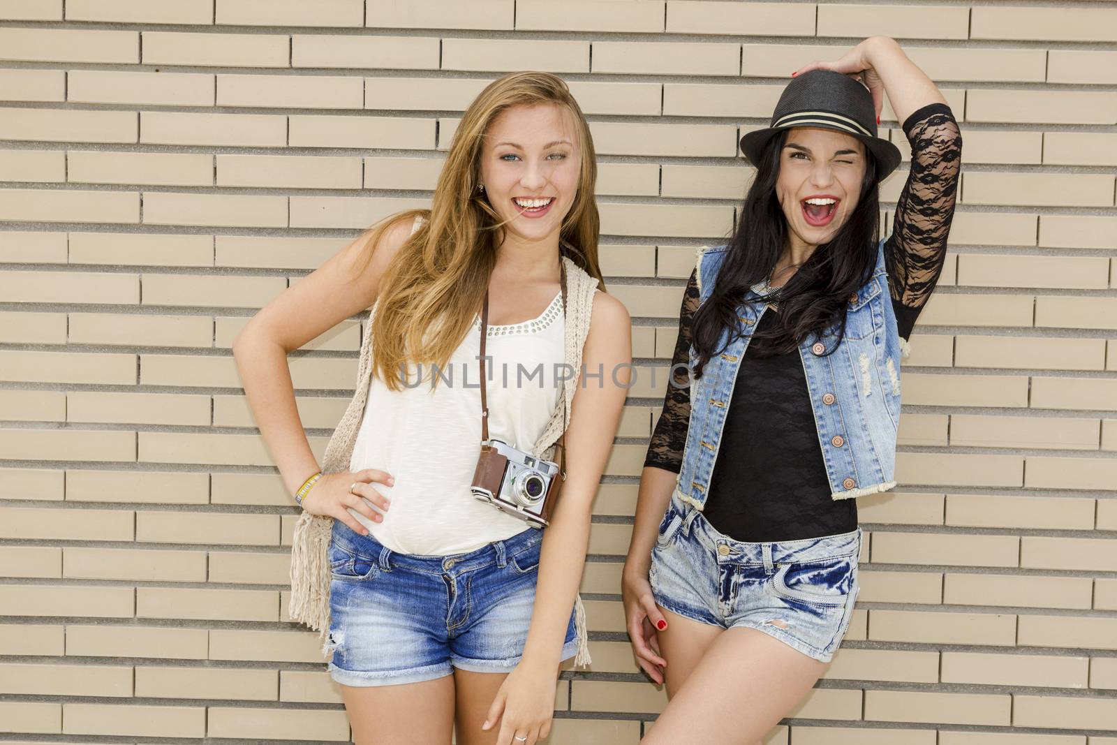 Two beautiful and young girlfriends having fun, in front of a brick wall