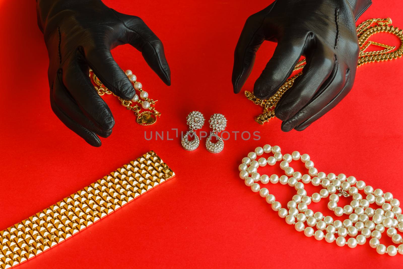 two hands wrapped in black gloves are going to steal  a set  of necklaces,bracelets and  earrings of gold  and diamonds  placed on a red background