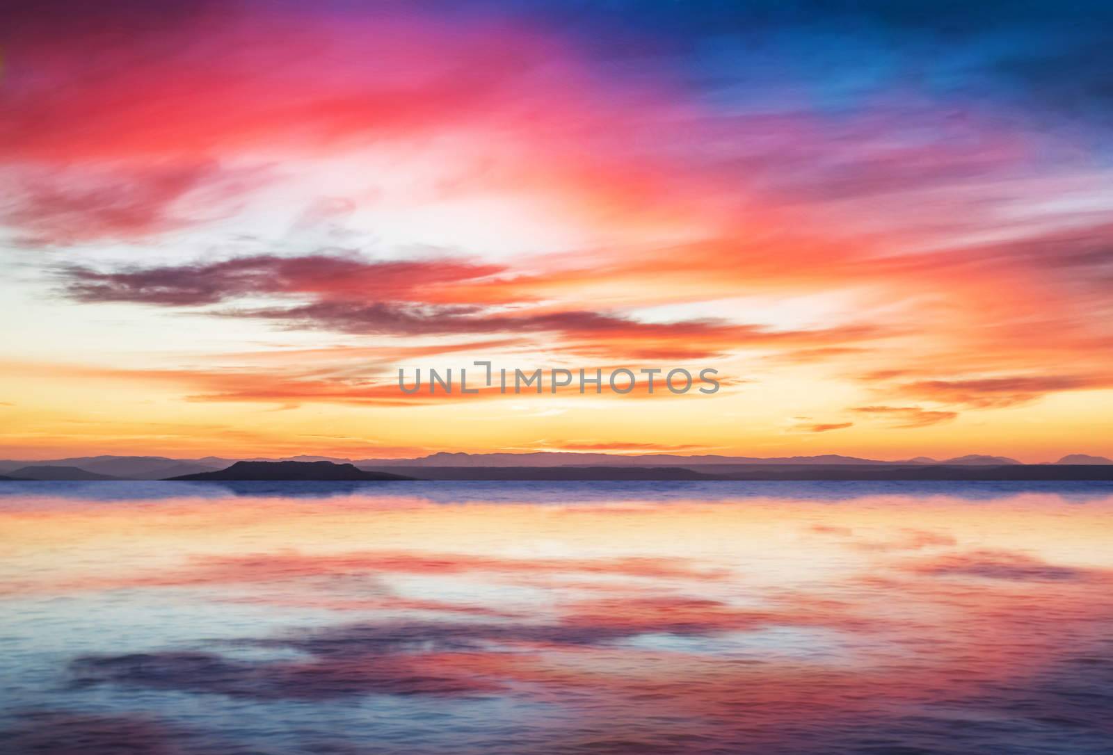 sunset scene on quiet sea with mountains in background, colorful sky with soft clouds