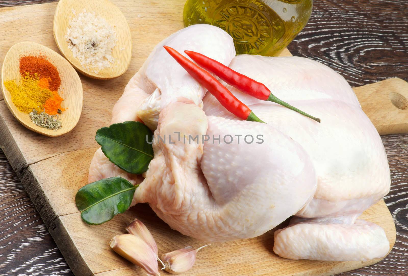 Perfect Raw Chicken Full Body Trussed and Ready to Roast with Chili Peppers, Hot Crushed Spices, Garlic, Curry Leaves and Olive Oil closeup on Wooden Cutting Board