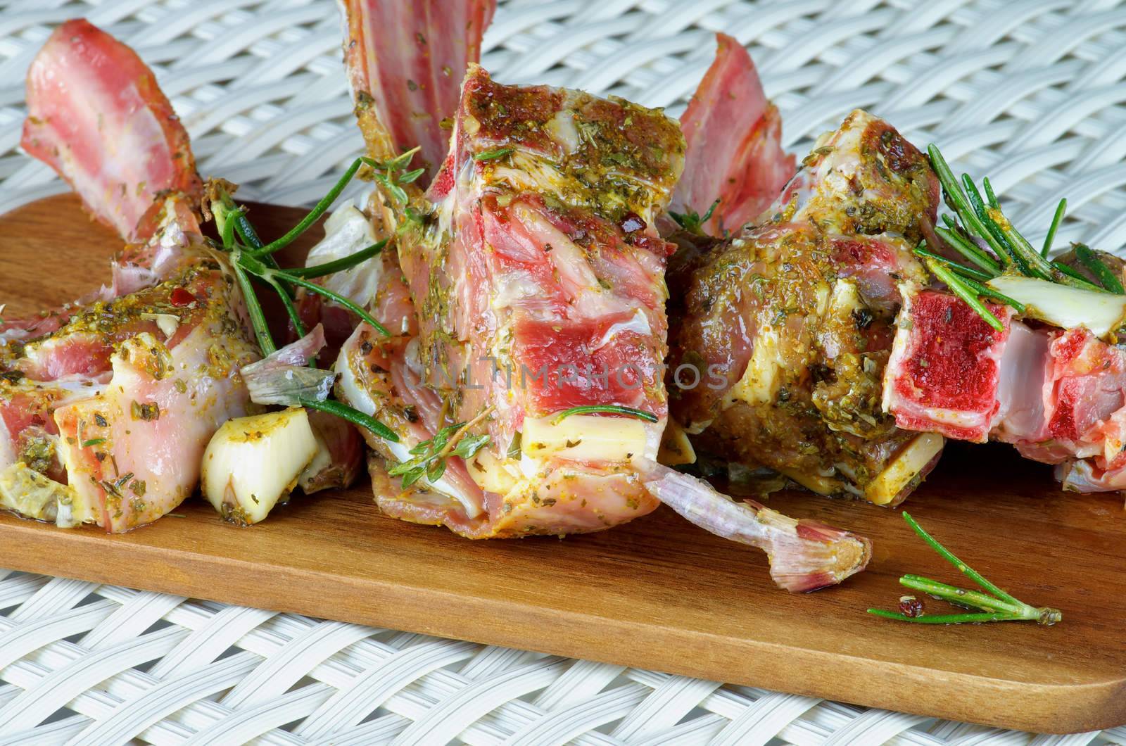 Delicious Raw Lamb Ribs in Marinade of Herbs and Spices with Rosemary and Garlic Ready to Roast closeup on Wooden Cutting Board