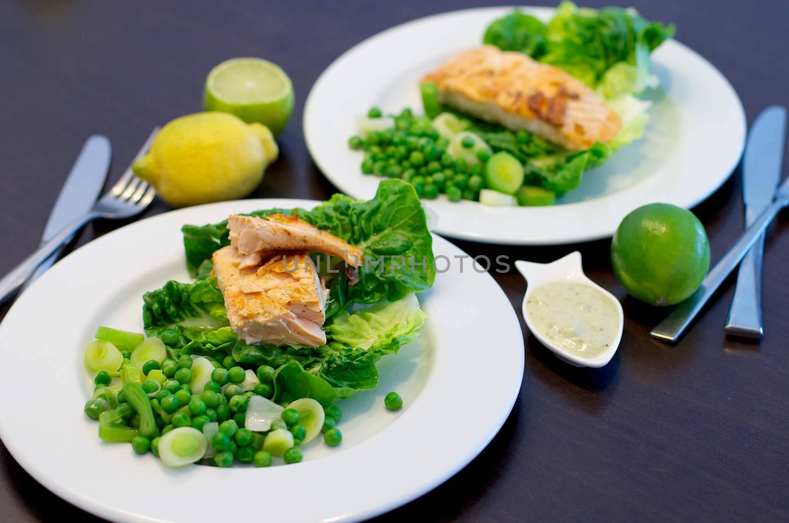 Delicious Roasted Salmon with Leek, Sweet Pea and Romano on White Plates closeup on Dark Wooden background. Focus on Foreground