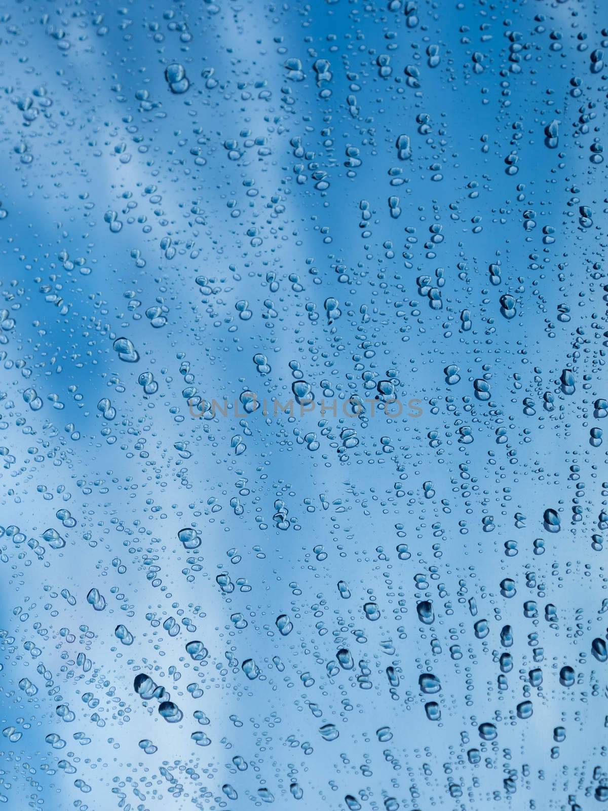 Image of droplets on window glass reflecting the blue sky.