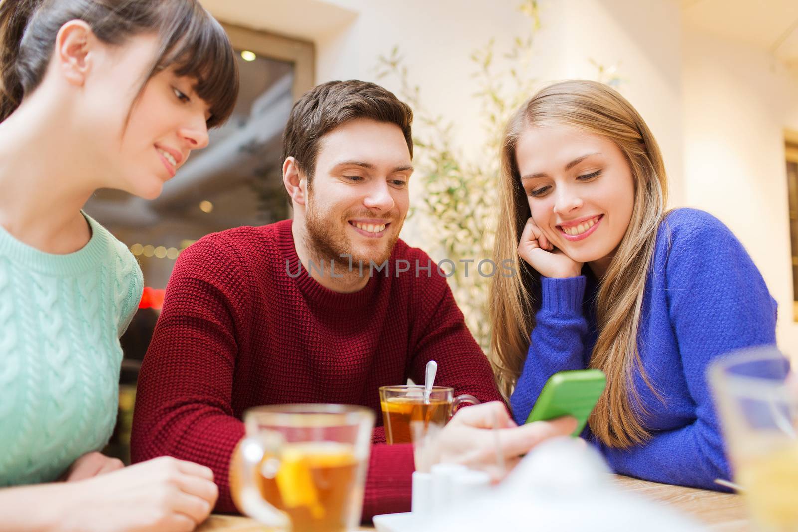 people, leisure, friendship and technology concept - group of happy friends with smartphone meeting at cafe and drinking tea